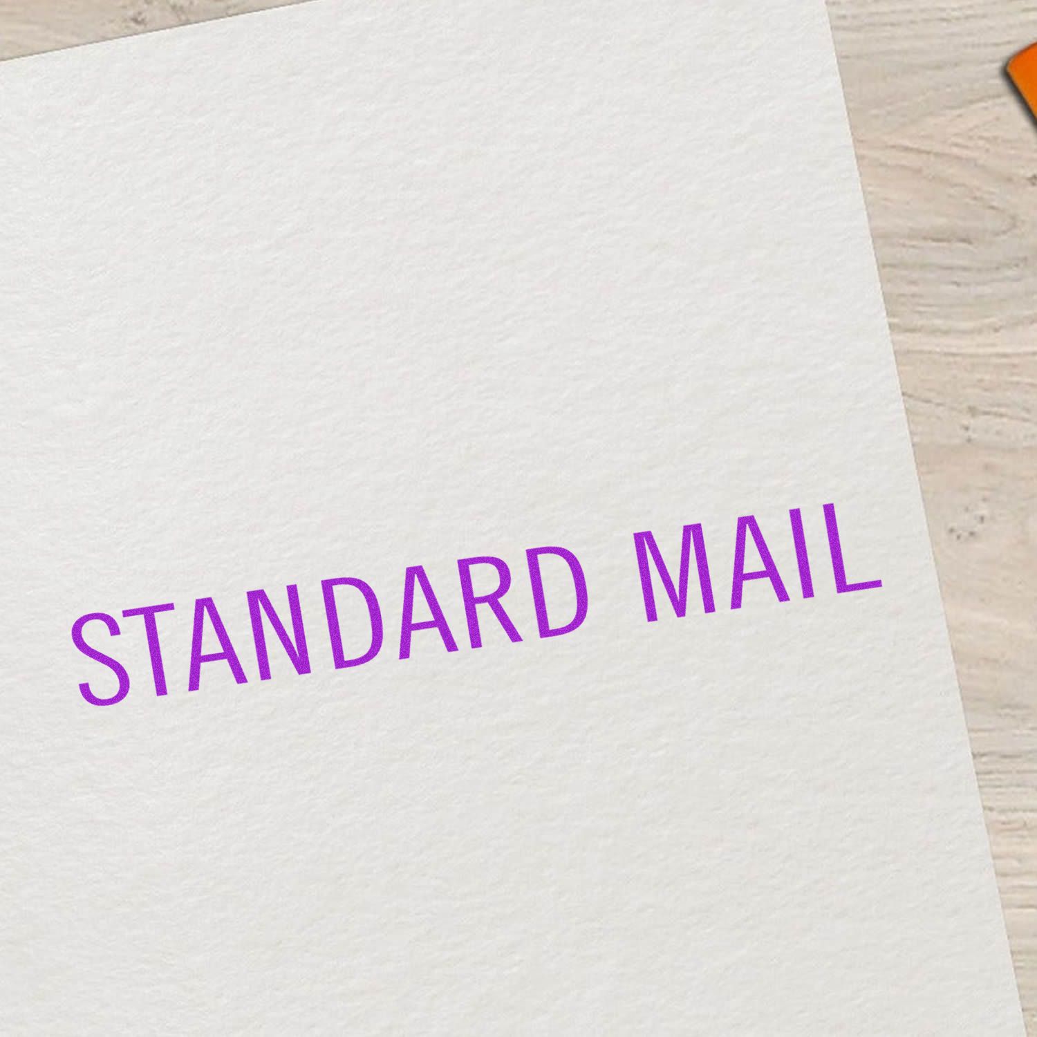 Close-up of a white envelope labeled Standard Mail in purple text on a light wooden surface.