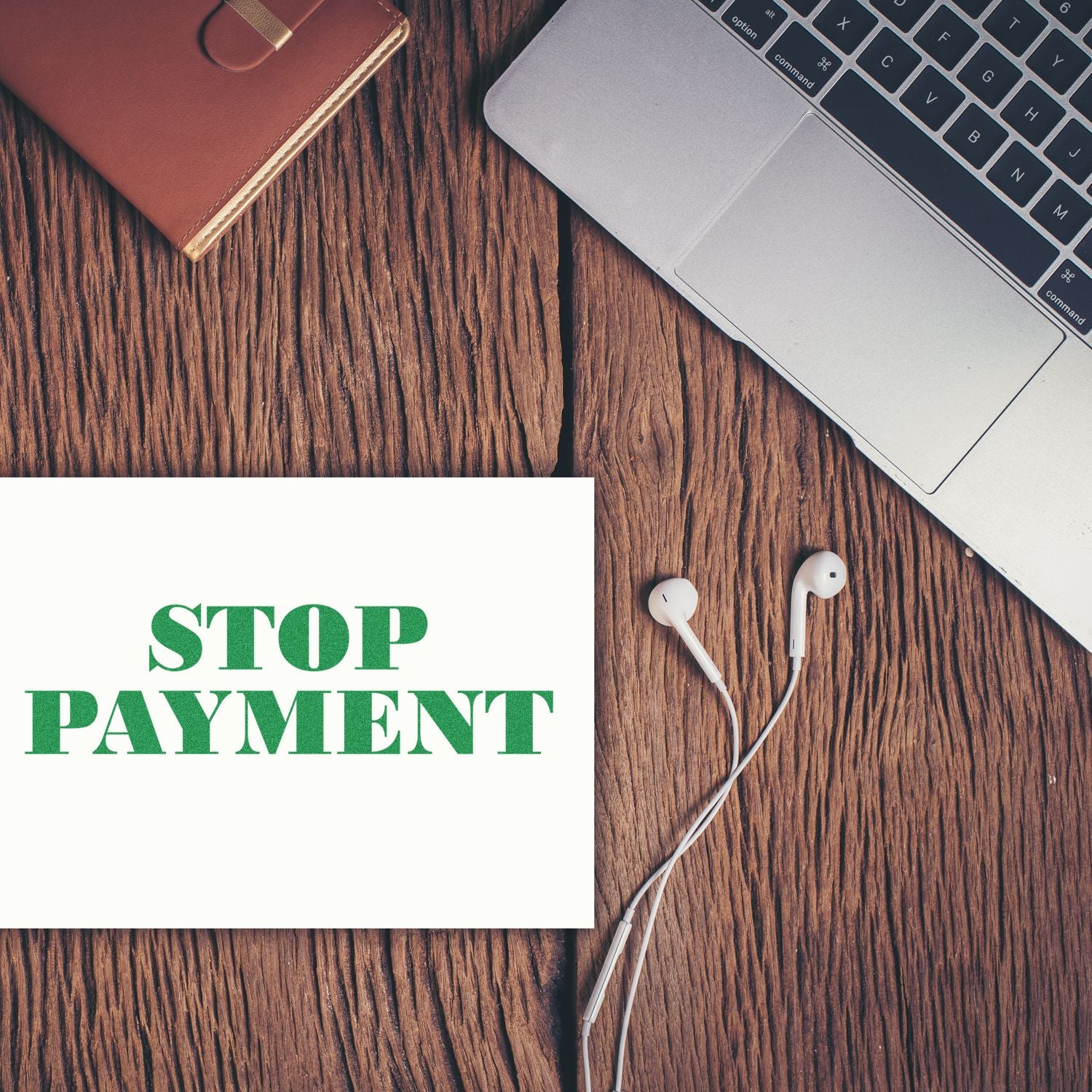 Laptop, earbuds, and Stop Payment sign on rustic wooden desk, representing online banking and payment cancellation.
