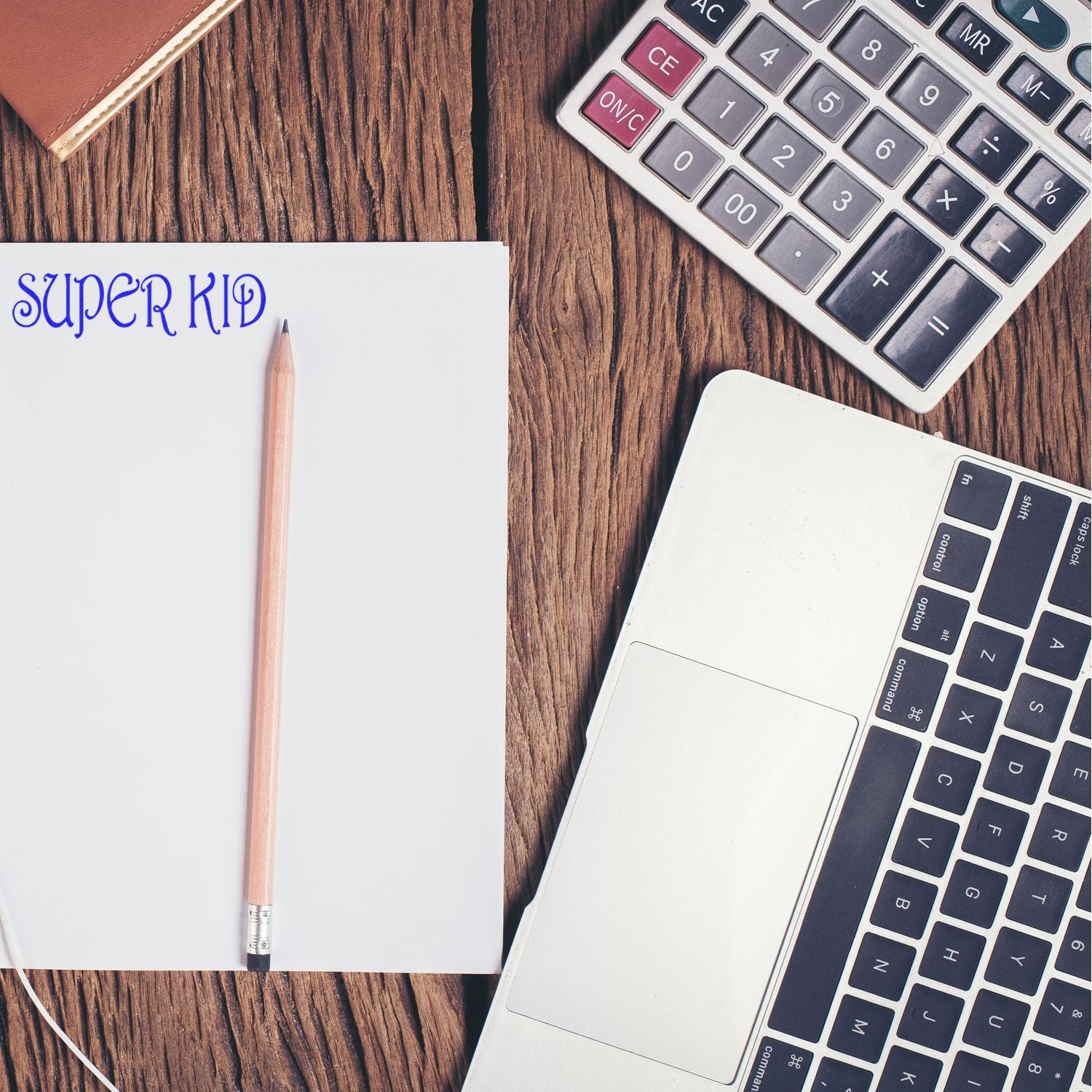 Notebook with Super Kid text, pencil, calculator, and laptop on a wooden desk, school and math concept
