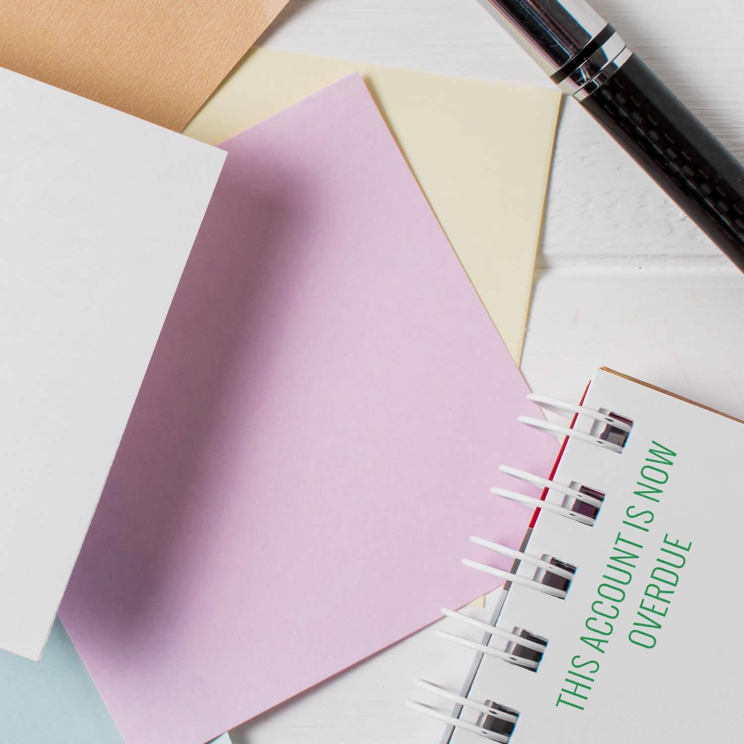 Colorful desk planner with sticky notes, pen, and spiral notebook showing This account is now overdue reminder.