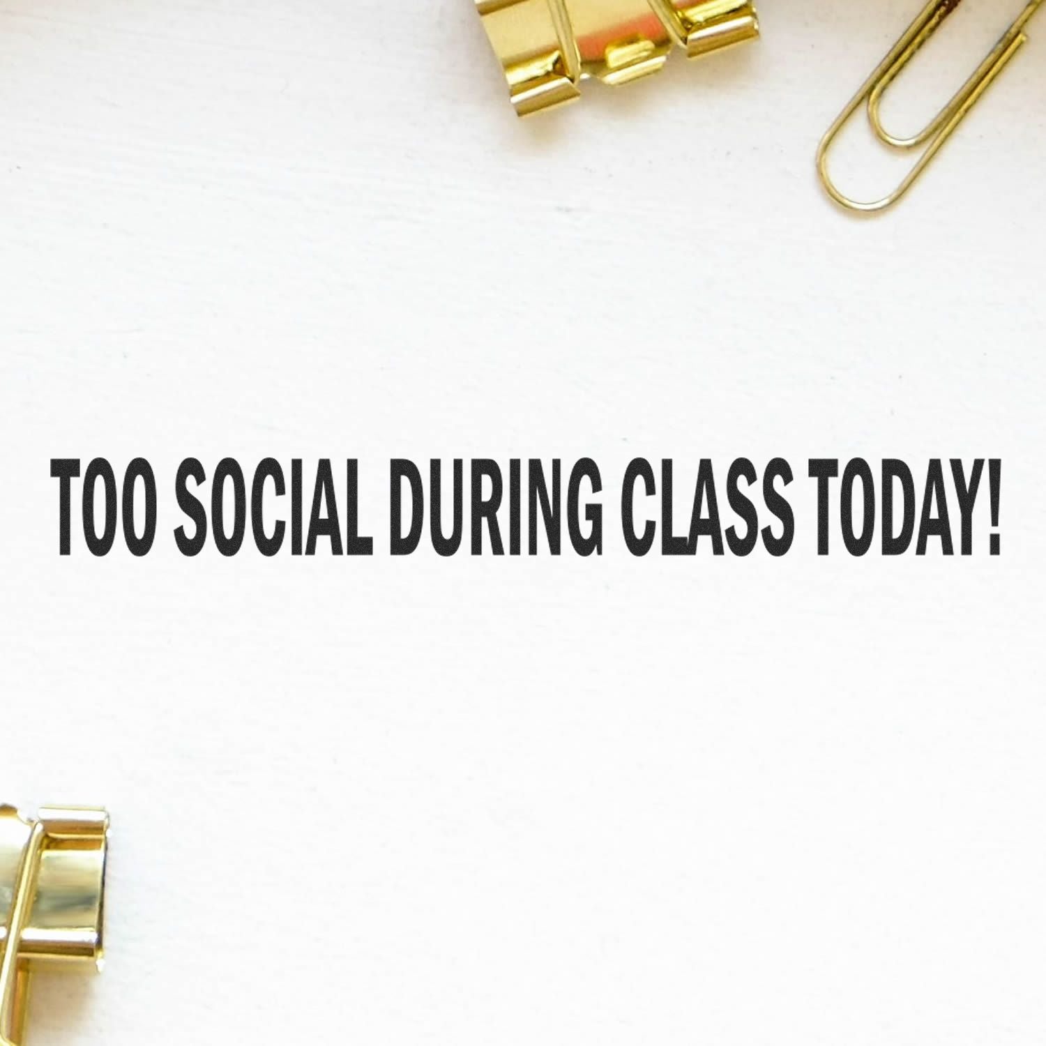 Minimal white desk flat lay with gold paper clips and bold text reading TOO SOCIAL DURING CLASS TODAY! for classroom or student motivation.