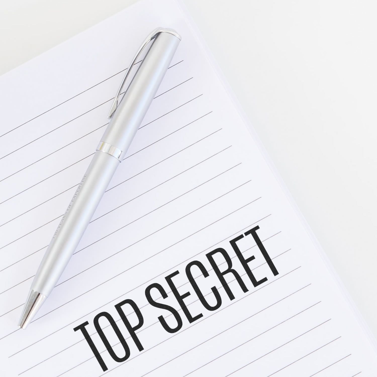 Silver pen on lined notebook paper with TOP SECRET text, concept of confidential business notes and secret information.