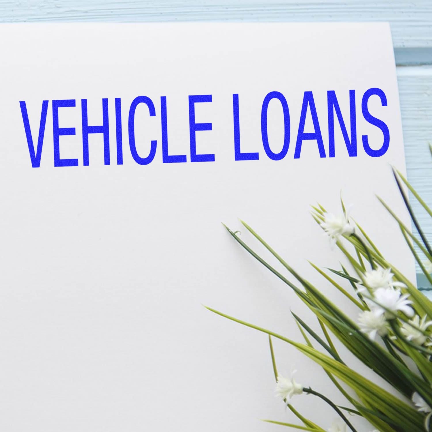 Vehicle loans promotional banner on white card with blue text and fresh green flowers, advertising vehicle financing for cars and trucks.