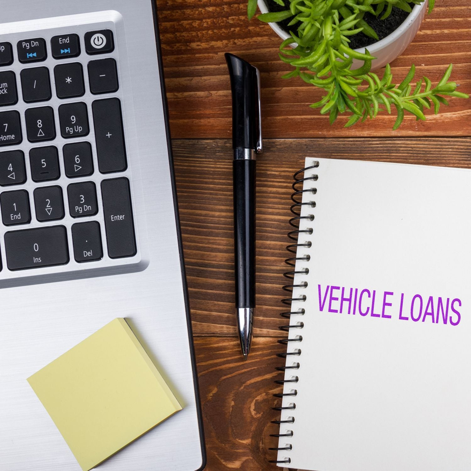 Vehicle loans concept with laptop keyboard, notebook, pen, and plant on wooden desk