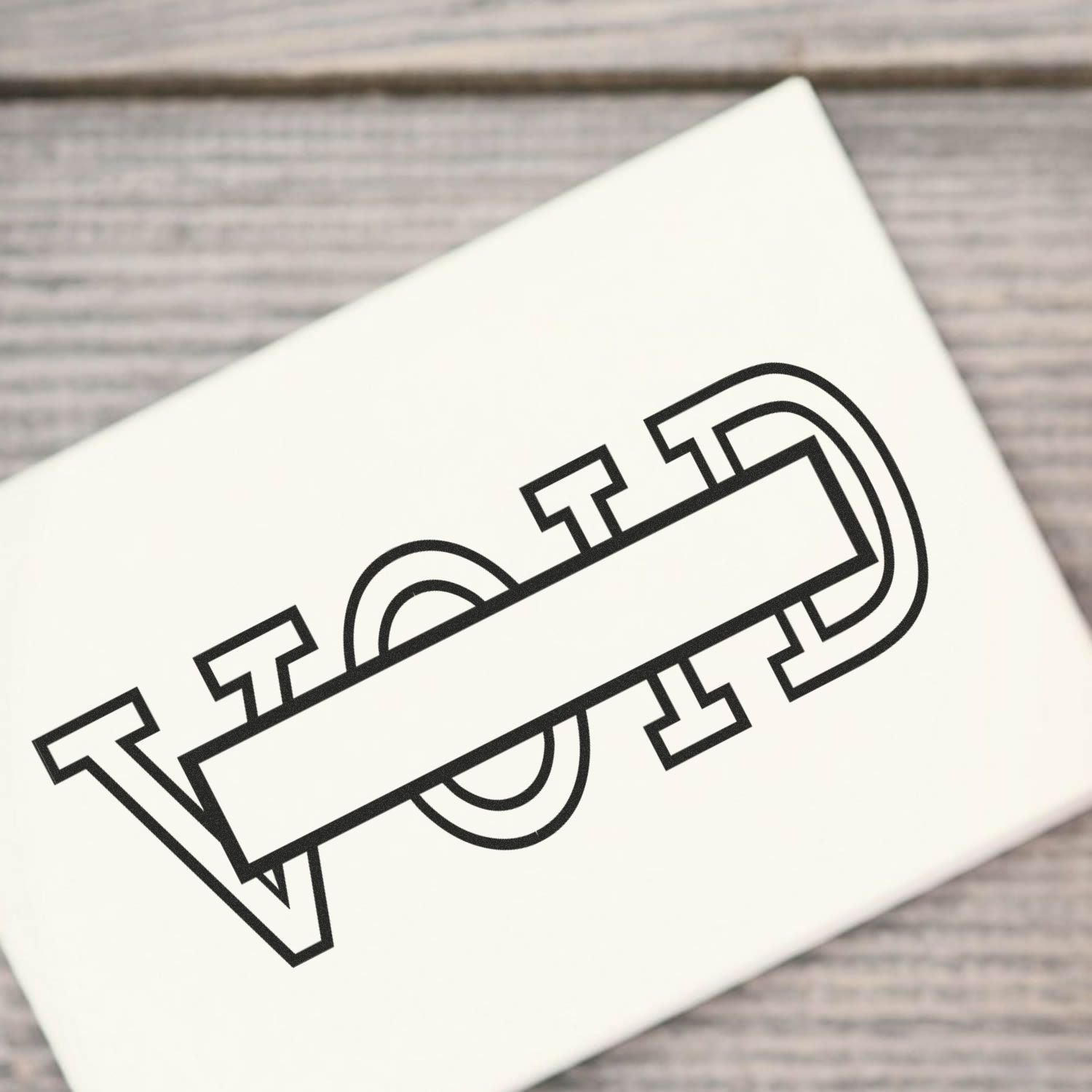Close-up of a white greeting card showing bold monoline typography logo on a rustic wooden background, for brand promotion.