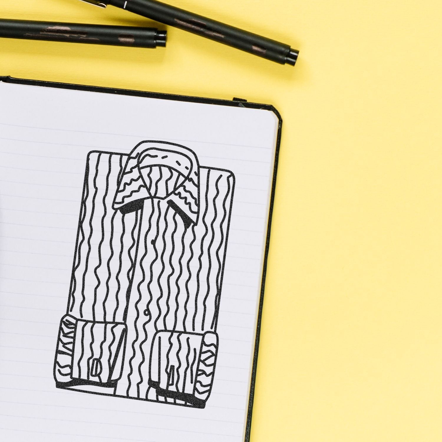 Hand-drawn backpack sketch in a notebook with black markers on a yellow background, creative stationery flat lay.