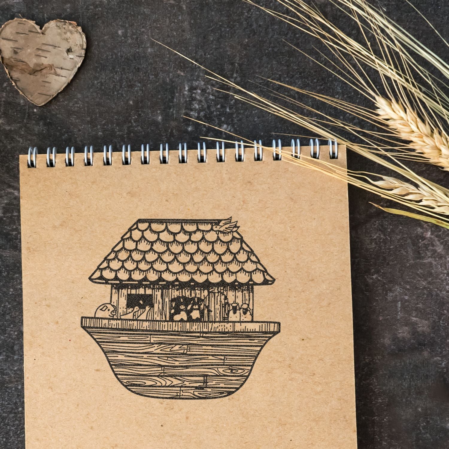 Rustic kraft spiral notebook with birdhouse illustration, dried wheat decor, and heart-shaped wood cutout on dark background