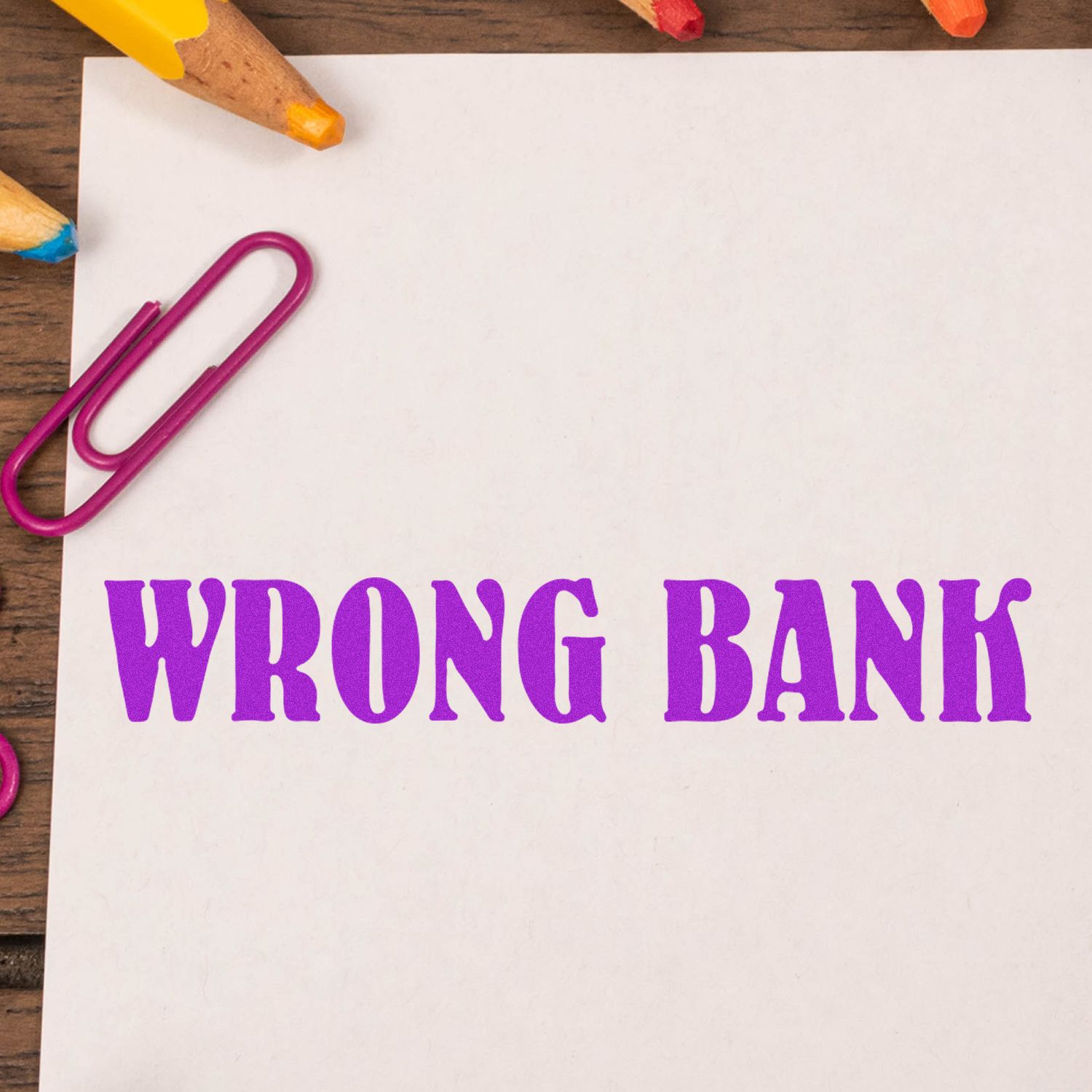 Wrong Bank purple text on white paper with colorful pencils and paper clips on a wooden desk.