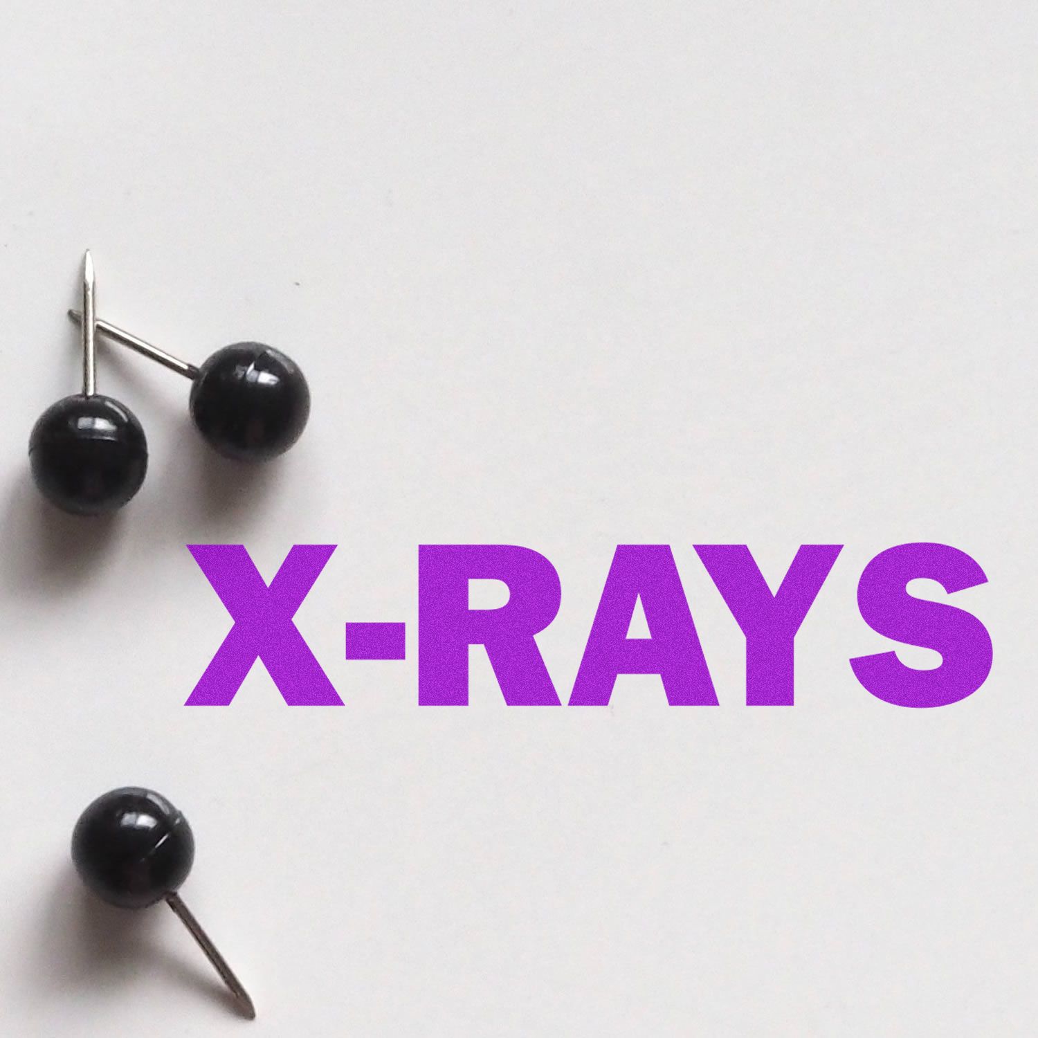 Purple X-RAYS text with push pins on a white background, medical imaging concept.