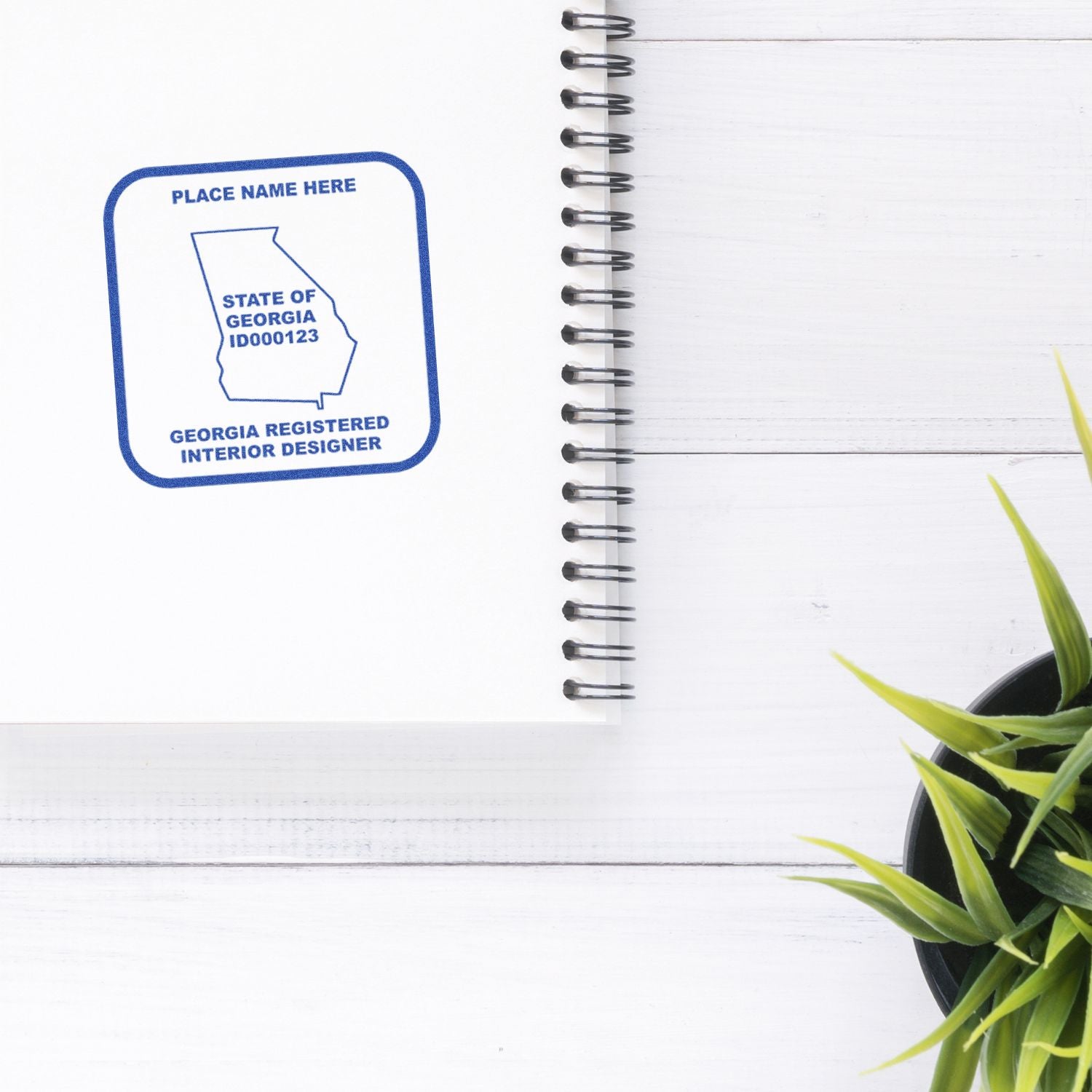 Georgia Registered Interior Designer logo on a spiral notebook with a potted plant on a white wooden desk.