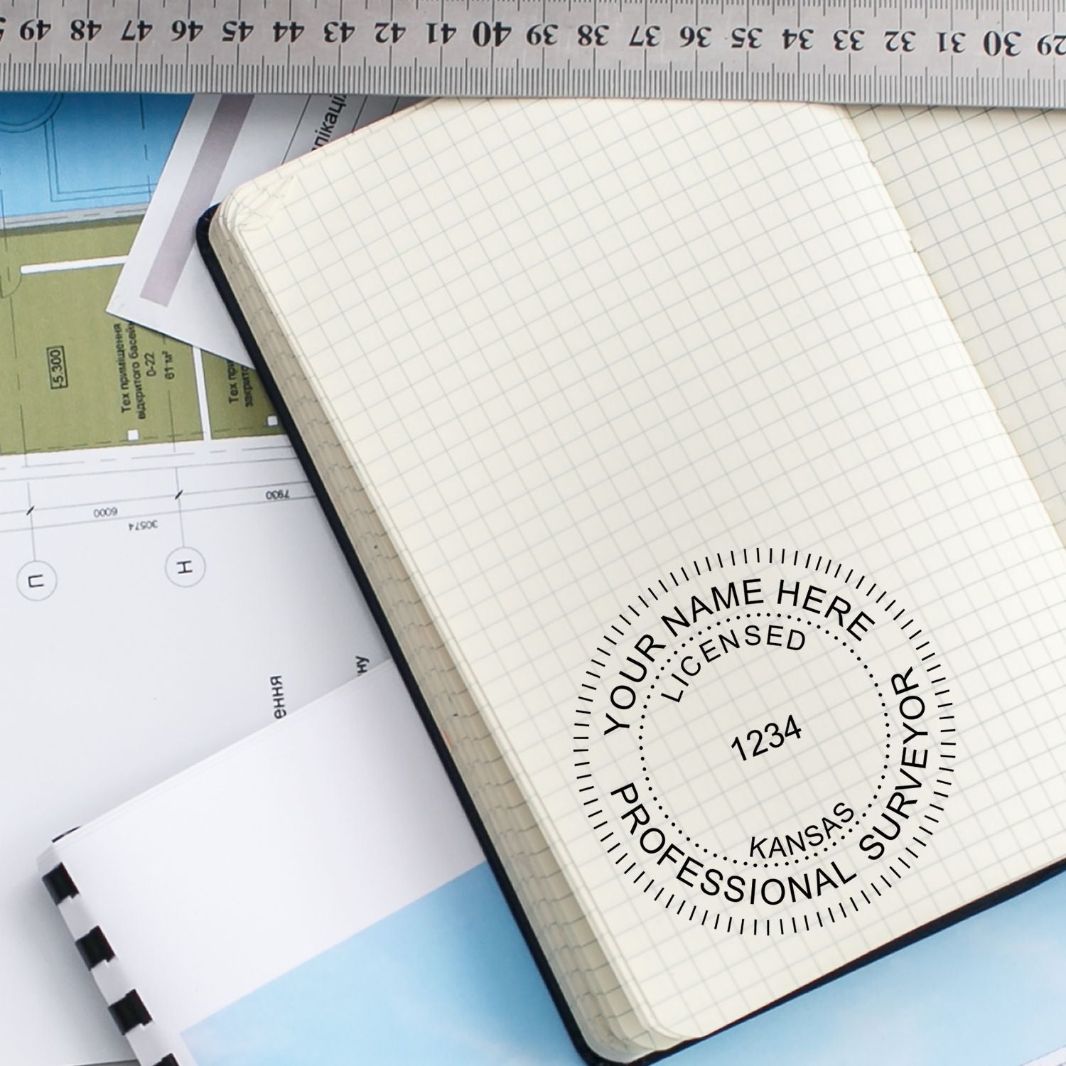 Top view of graph notebook, ruler, and survey plans with professional surveyor logo on a desk.