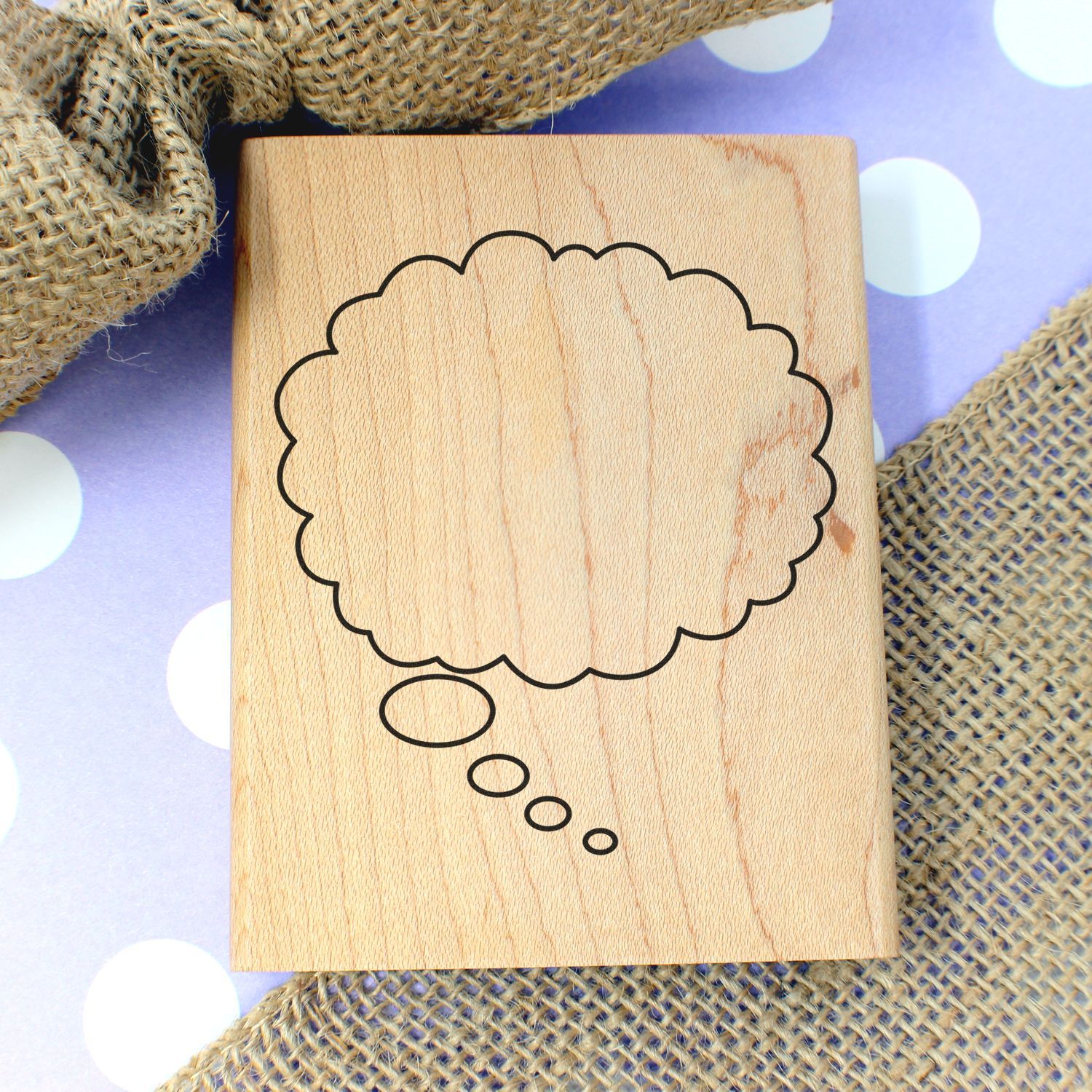 Wooden stamp block with thought bubble outline on purple polka dot background and burlap fabric texture