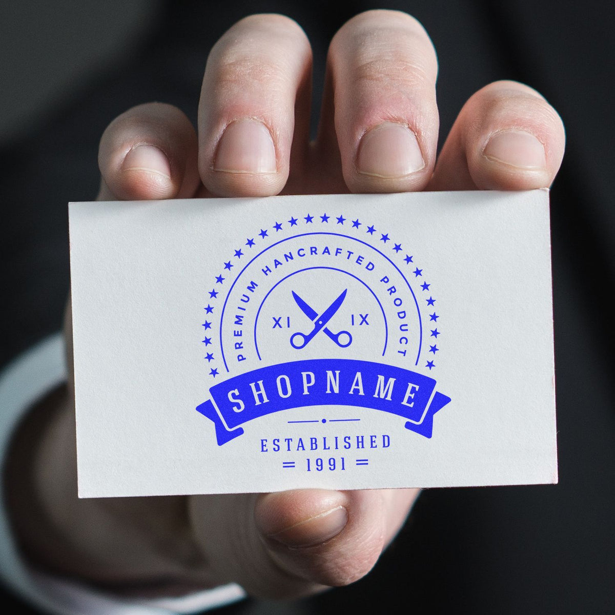 Hand holding a premium handcrafted business card logo for Shopname, established 1991, with blue scissors emblem on white background.