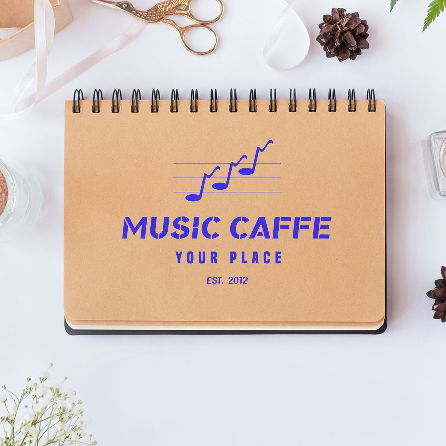 Top view of Music Caffe Your Place notebook with musical notes and EST. 2012 branding on kraft paper.