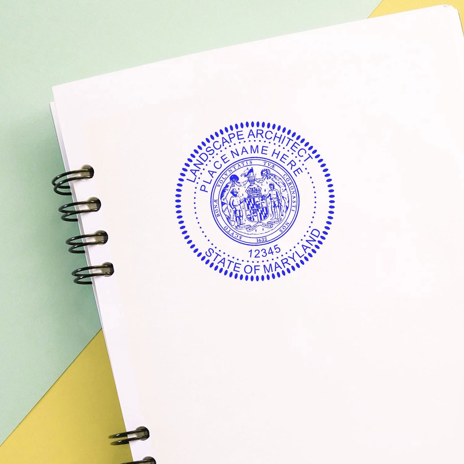 Maryland landscape architect seal stamped on a white spiral notebook page with office paperwork background.