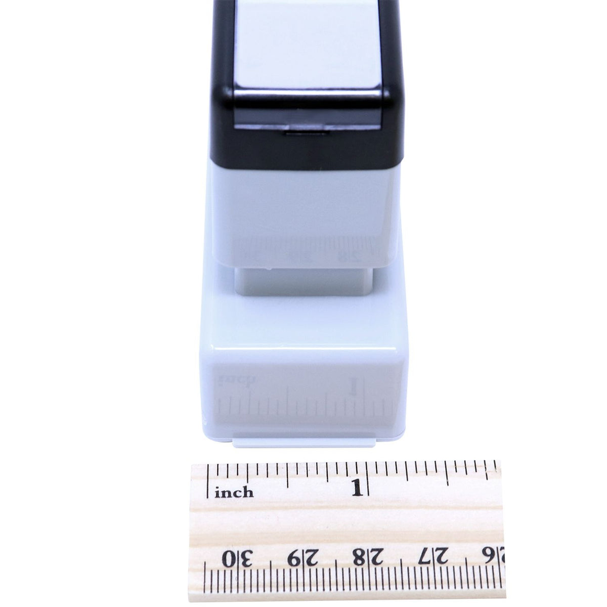 Close-up of compact white handheld device with black top, shown next to an inch ruler for size measurement