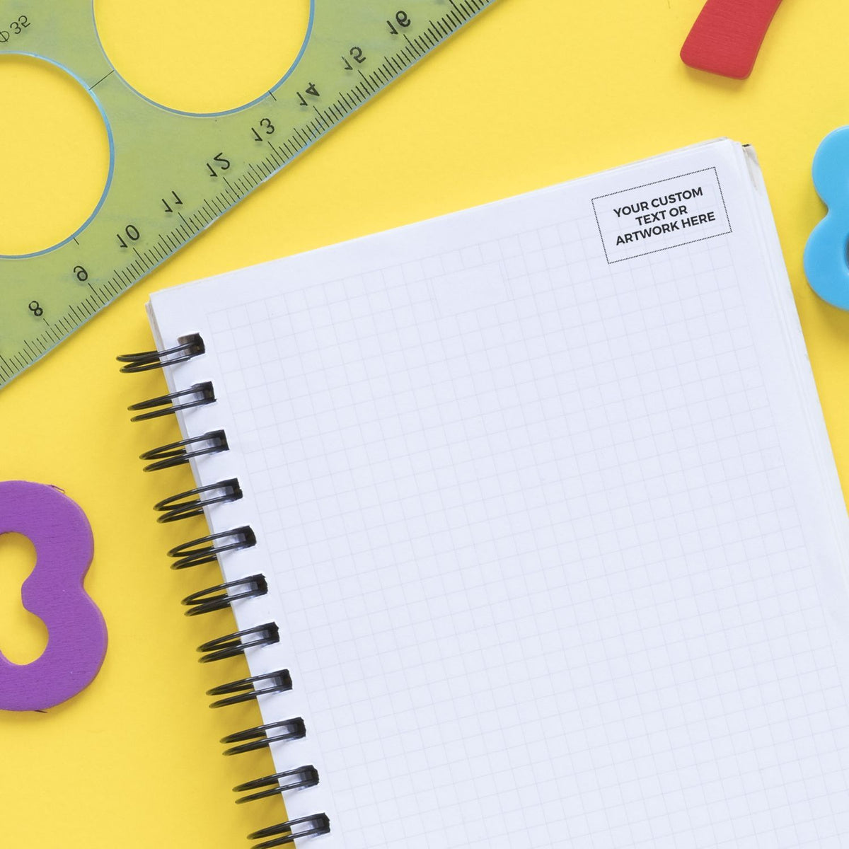 Blank grid notebook template for custom text, with ruler and classroom supplies on yellow background for school writing designs.
