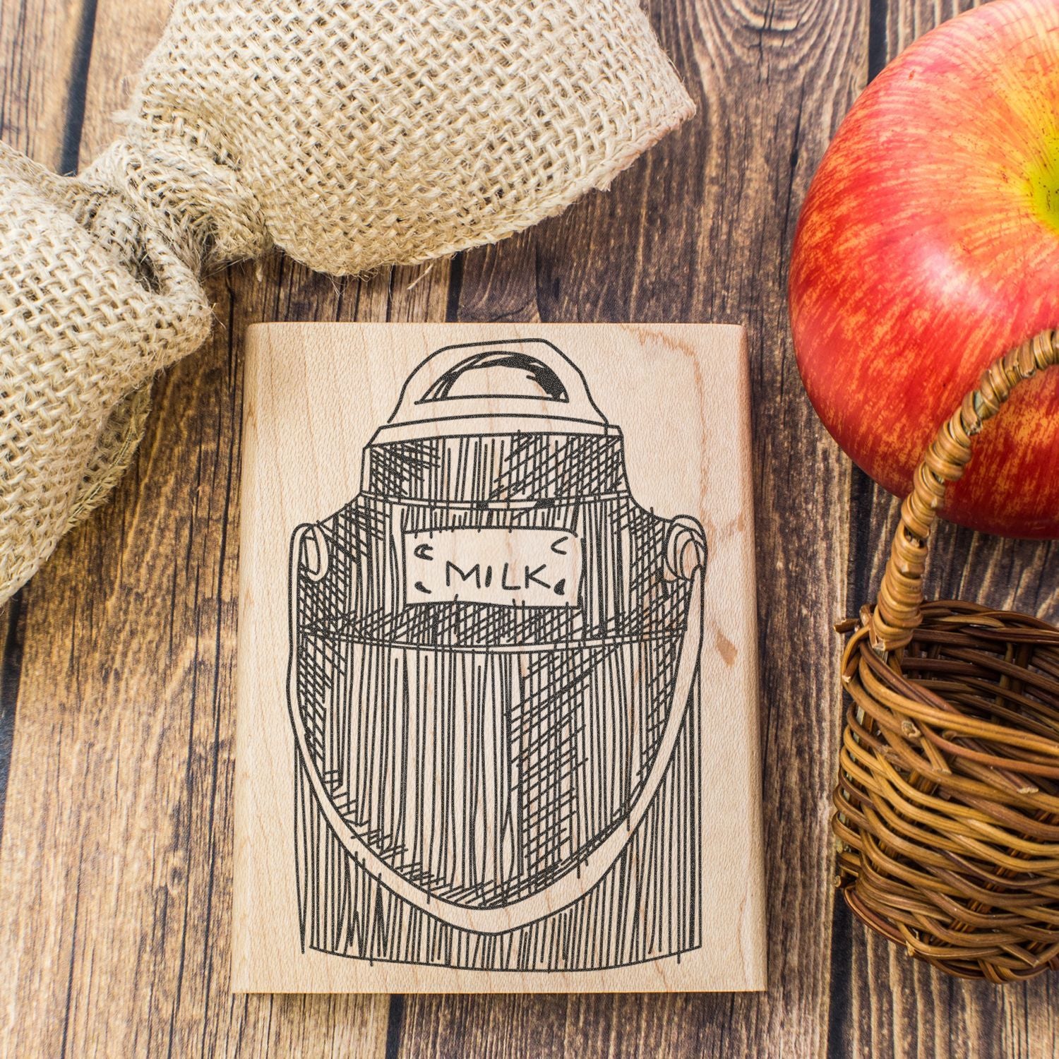 Rustic wooden milk can stamp with apple, burlap, and wicker basket on a farmhouse wood background