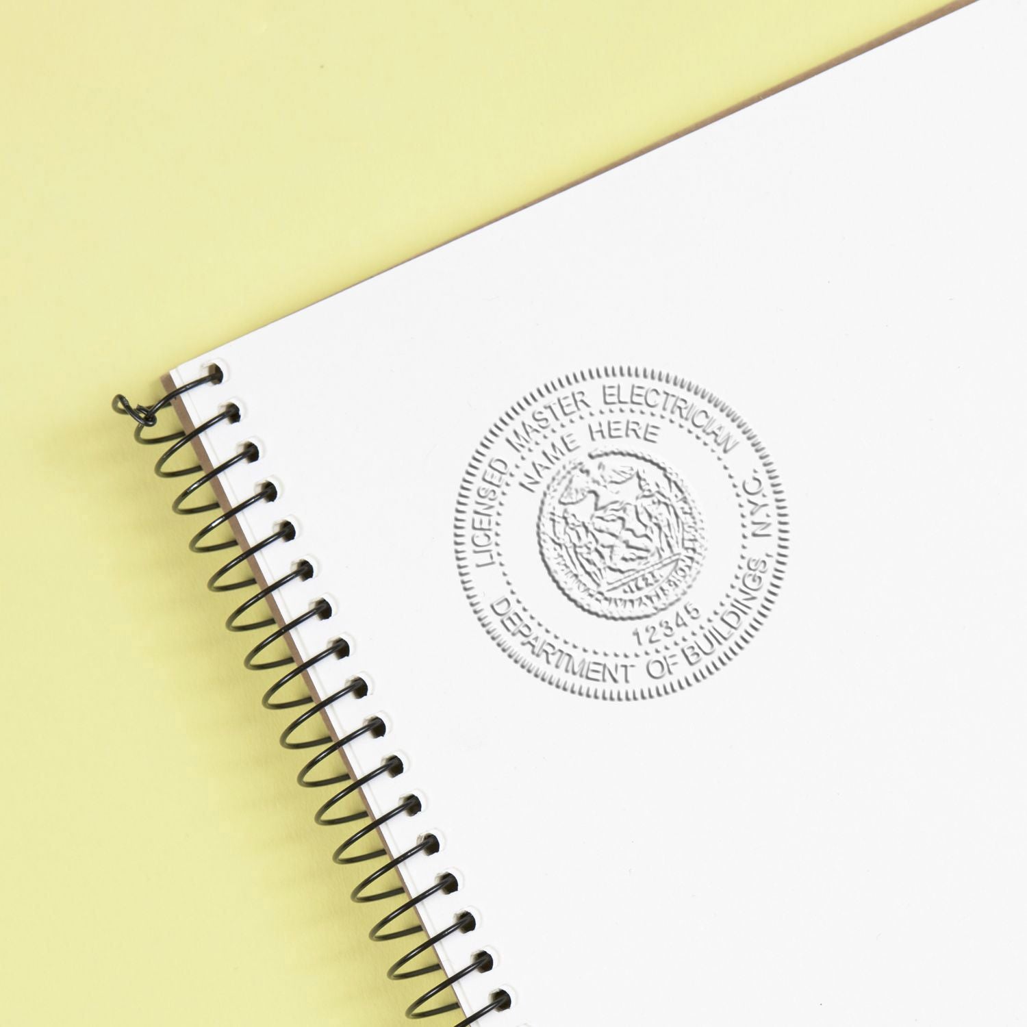 White spiral notebook with embossed Licensed Master Electrician seal on a yellow background.