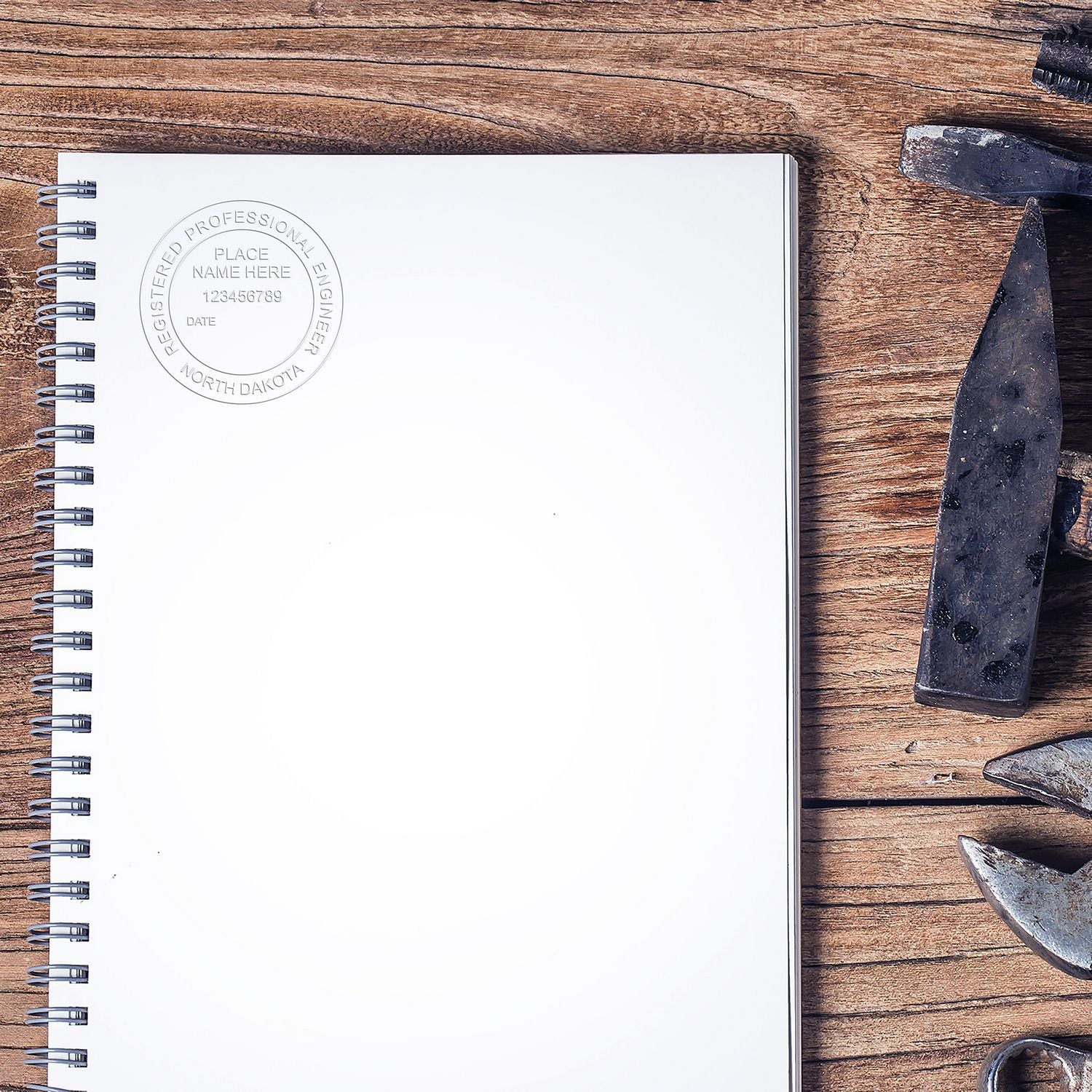 Blank spiral notebook with Registered Professional Engineer seal on rustic wooden desk, surrounded by geology hammer and rock samples.