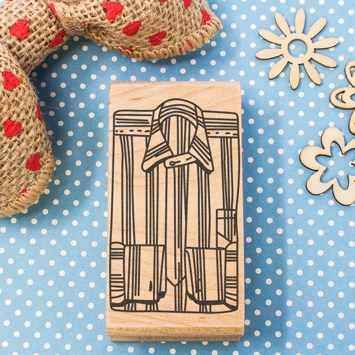Wooden rubber stamp with vintage clothing line art on a blue polka dot craft background with rustic burlap accents.