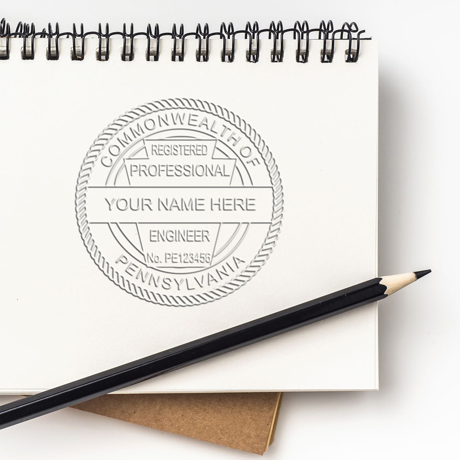Embossed professional engineer seal in a sketchbook with pencil, custom Commonwealth of Pennsylvania registered engineer stamp design.