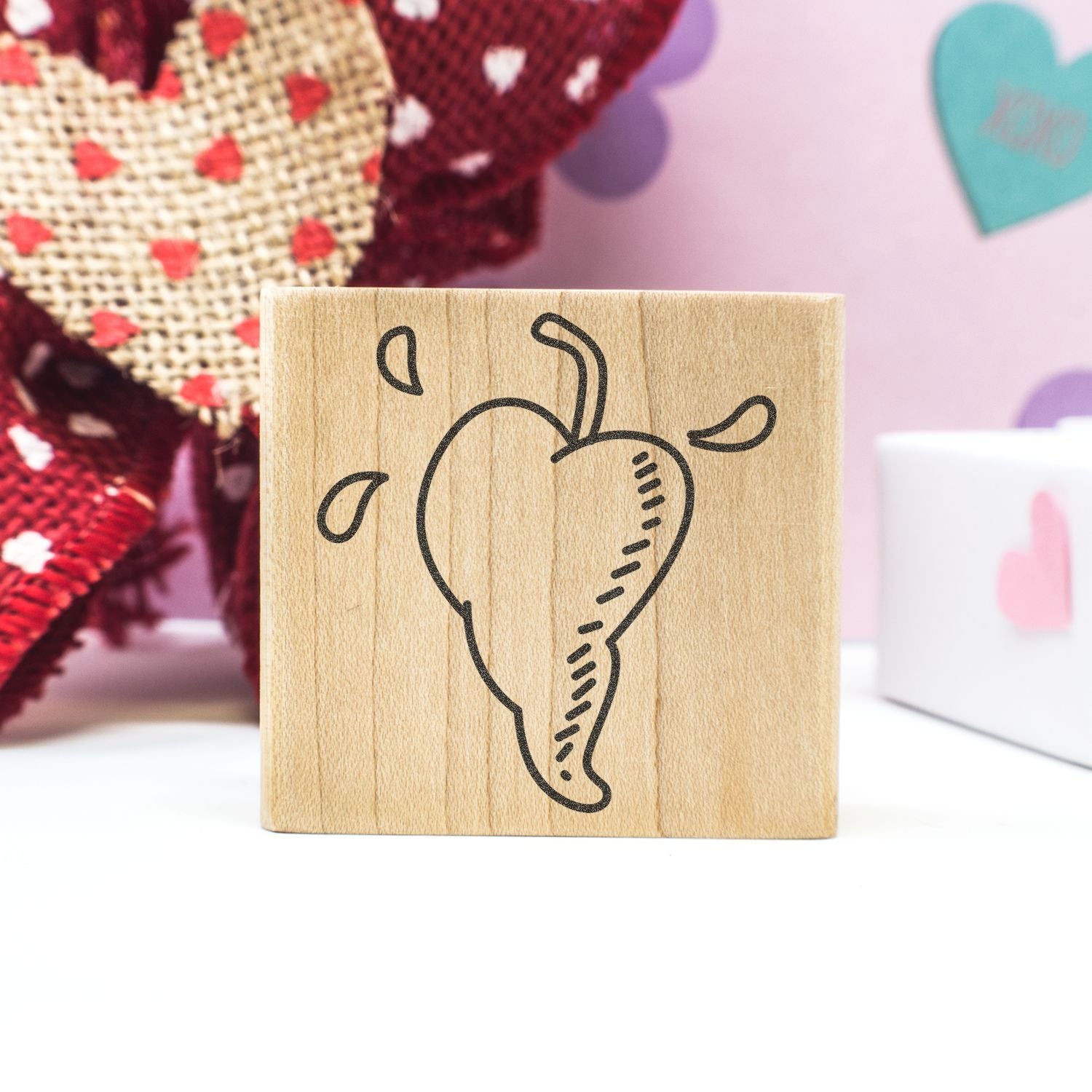 Wooden heart stamp on a craft block with Valentine decorations and pastel background.