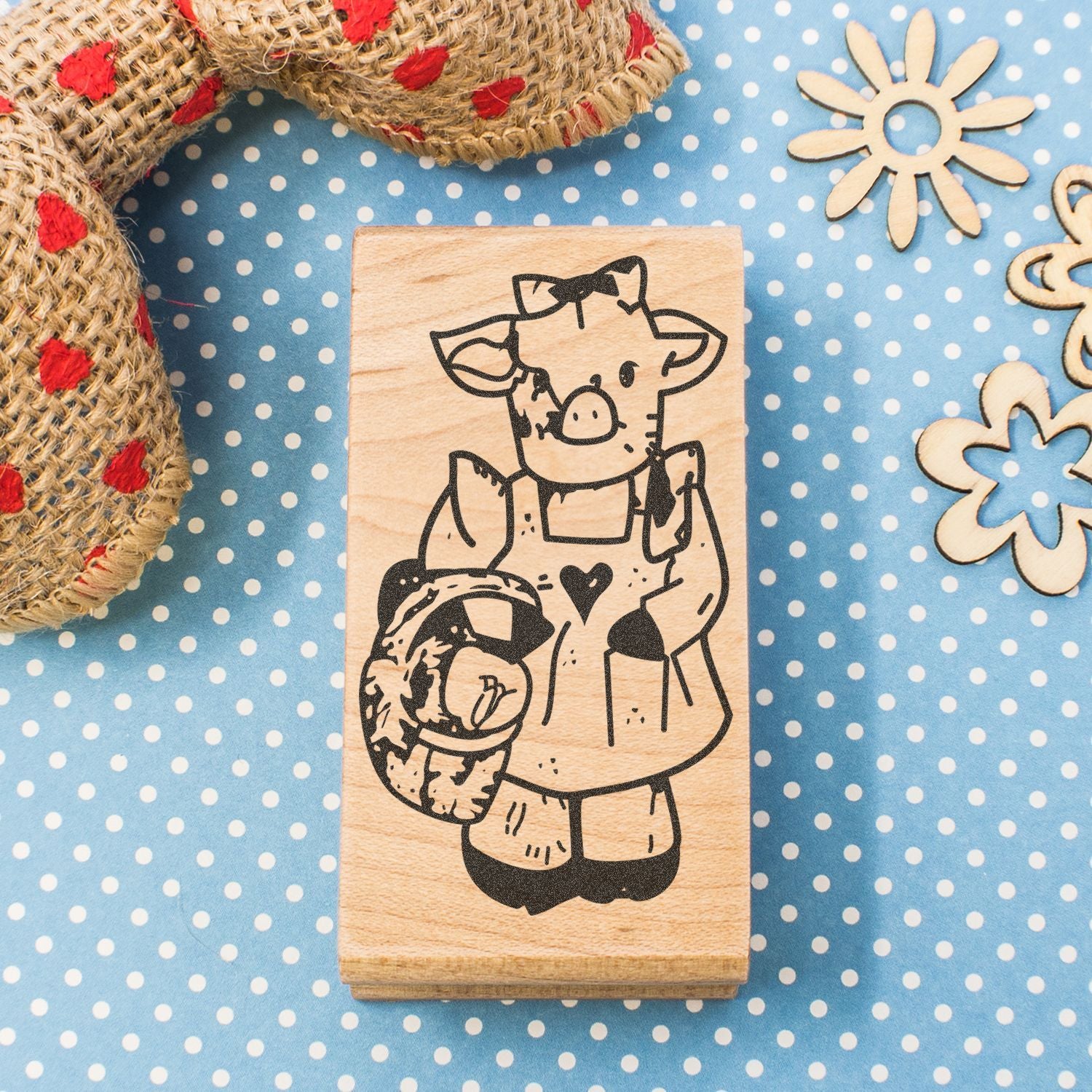 Handmade wooden stamp with cute cow illustration on blue polka dot background, rustic craft accessory with decorative rope and floral cutouts
