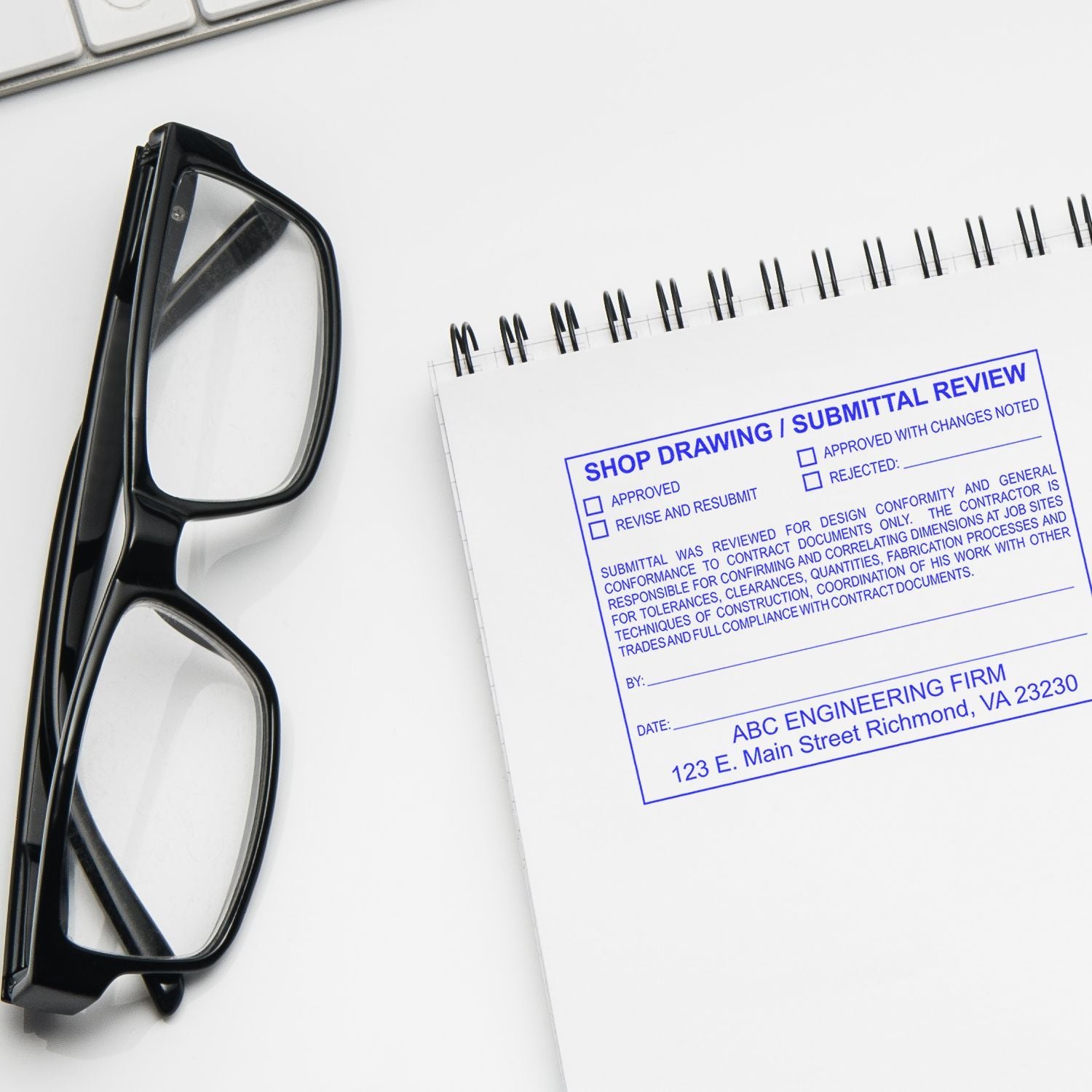 Black eyeglasses beside a shop drawing submittal review document on a white desk for an engineering firm.