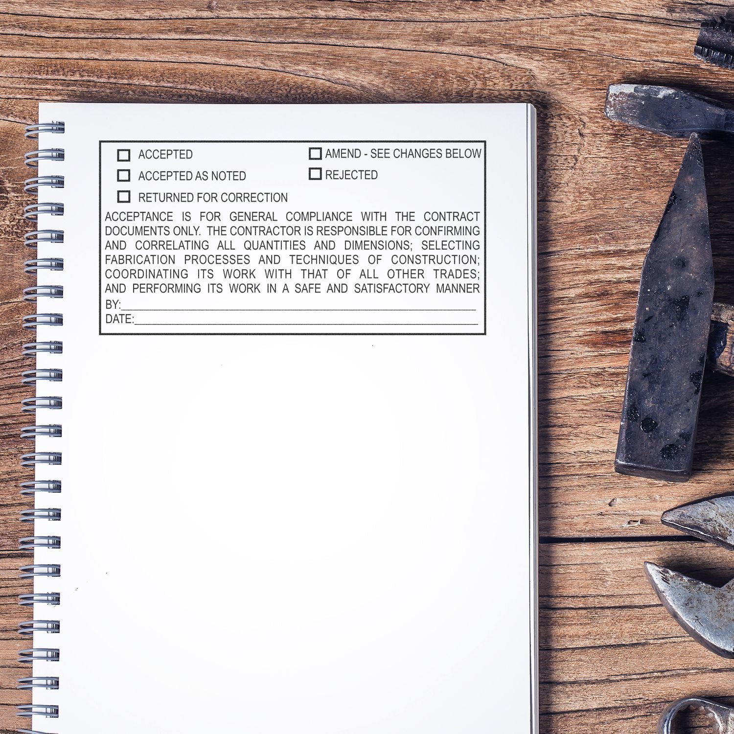 Spiral notebook with construction contract approval form on rustic wooden table with metal tools.