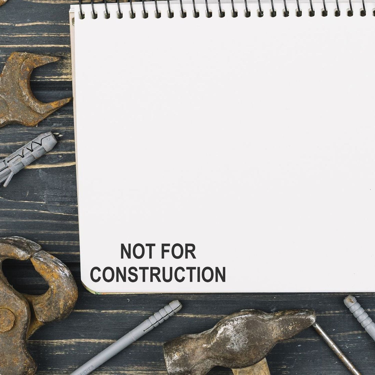 Blank spiral notebook with Not for Construction text, surrounded by construction tools on a dark wooden background.