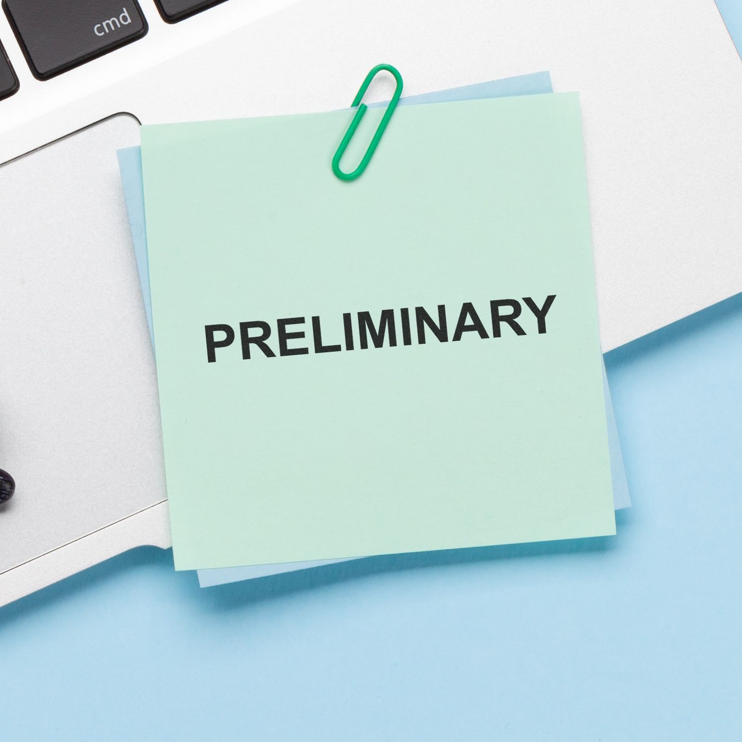 Preliminary note clipped to office documents beside a laptop keyboard, business paperwork concept.