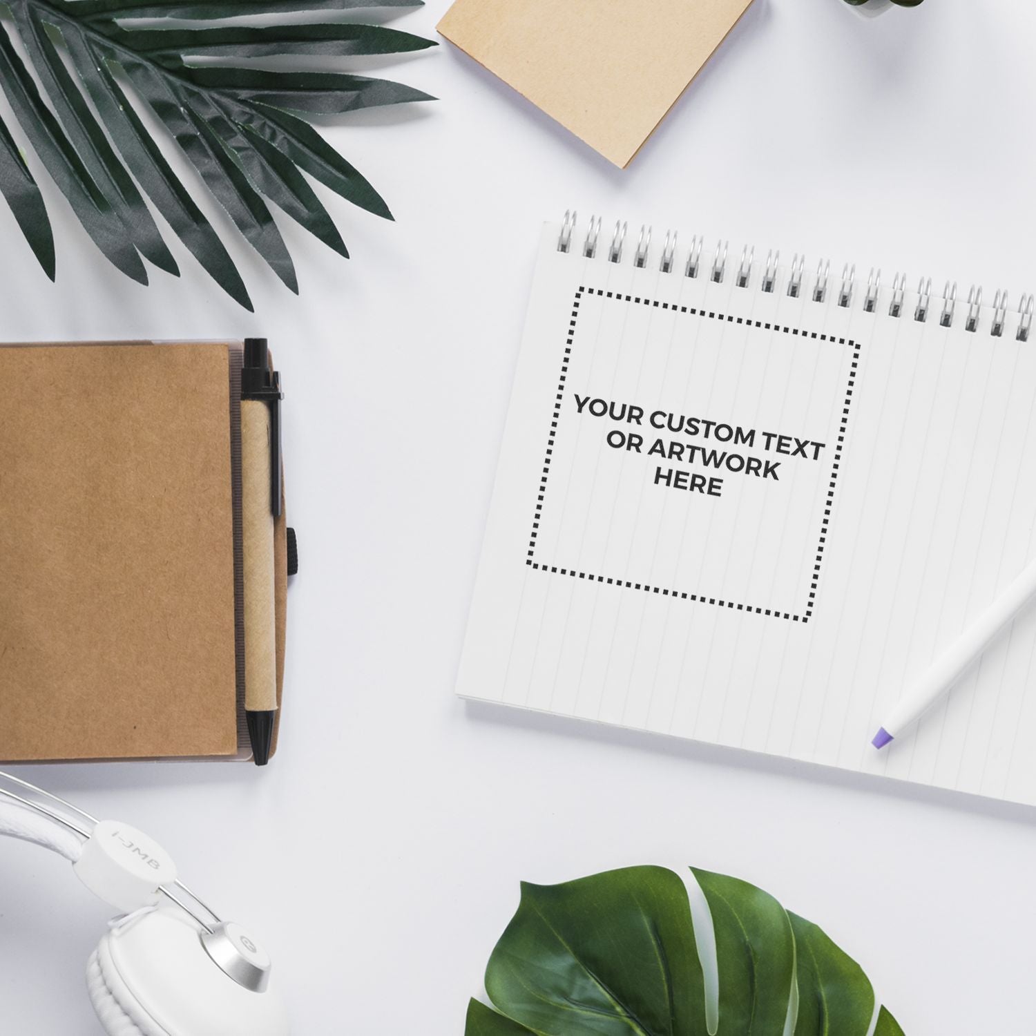 Top view of custom text notebook mockup on desk with pen, headphones, and plant leavesideal for branding and stationery design.