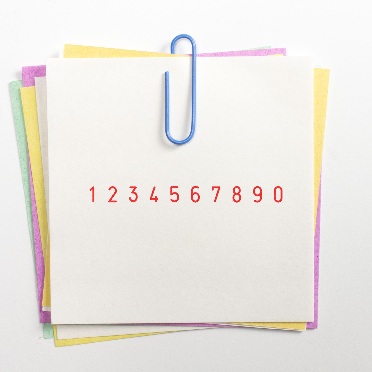 Stack of blank colorful note papers clipped with a blue paper clip, featuring red numbers 1 to 0 on white paper.