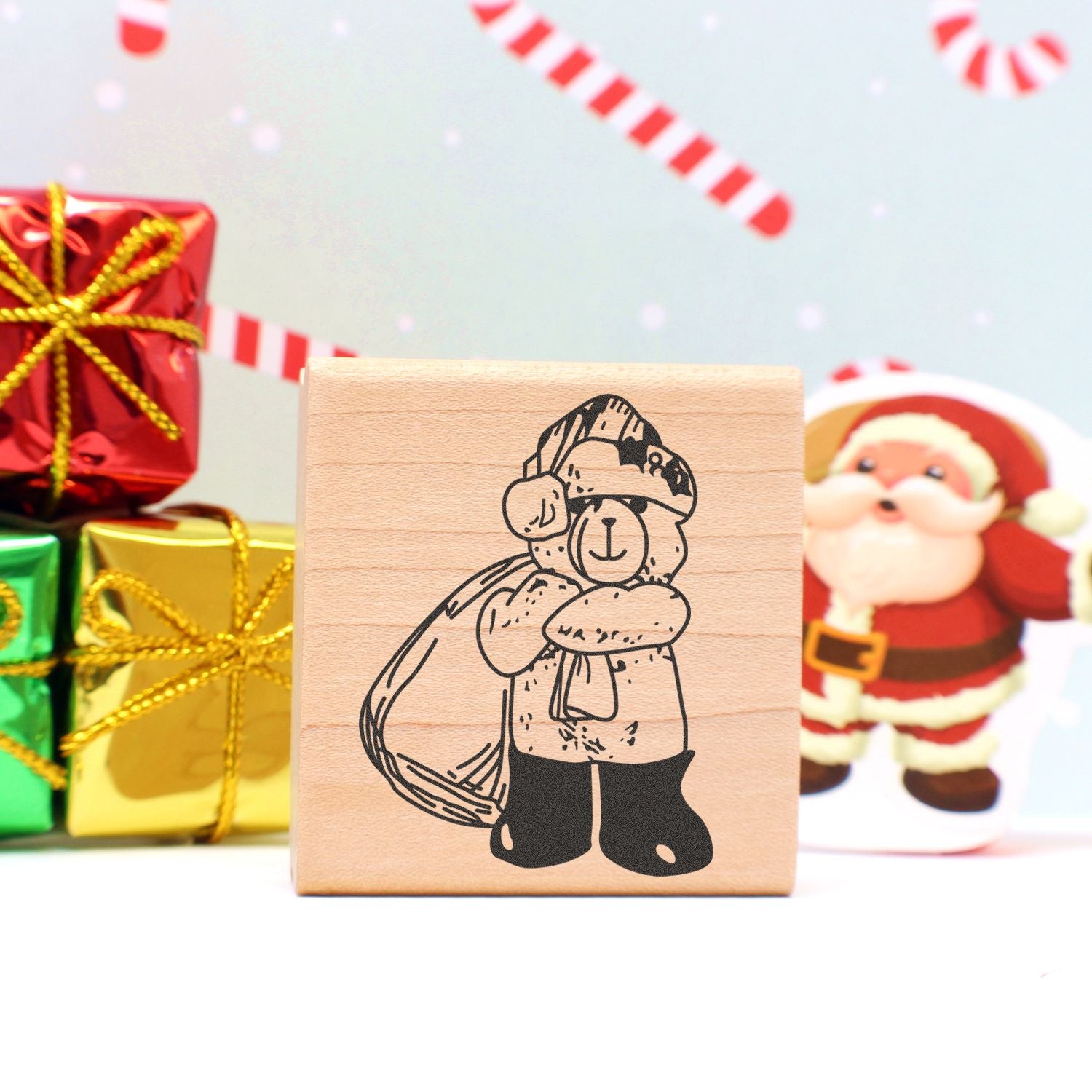 Wooden Christmas rubber stamp with a bear in a Santa hat, surrounded by festive gift boxes and holiday decor.