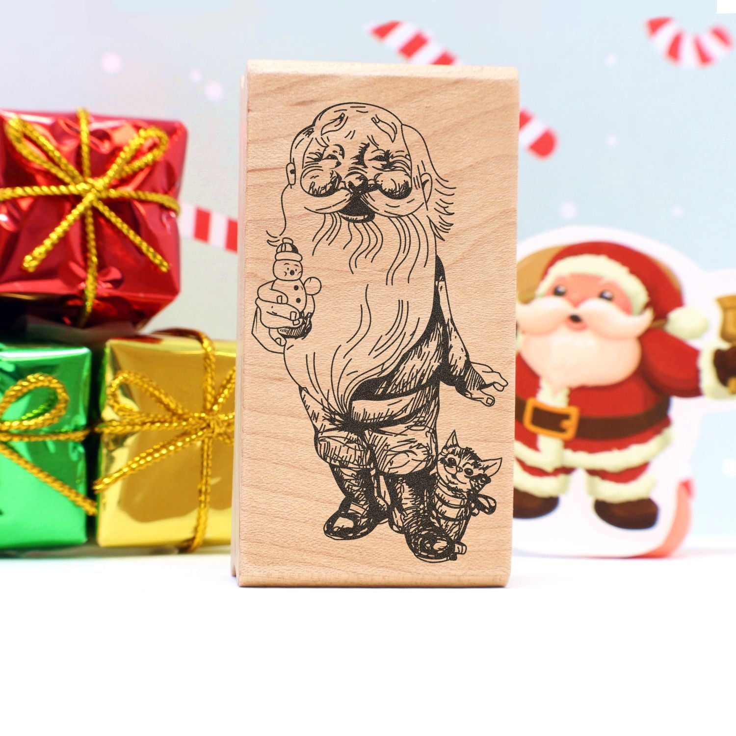 Wooden Christmas stamp with Santa and cat illustration, surrounded by festive holiday gift boxes and decorations.