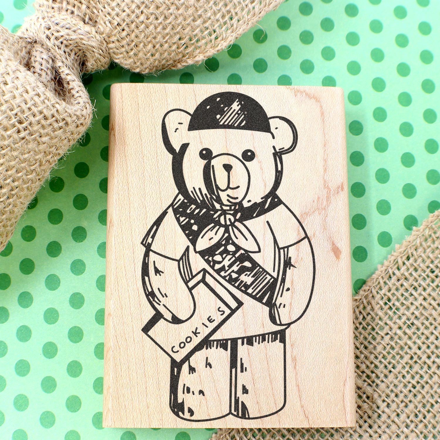 Wooden bear cookie stamp on green polka dot background with burlap decor, featuring a cute teddy bear holding a cookie box.