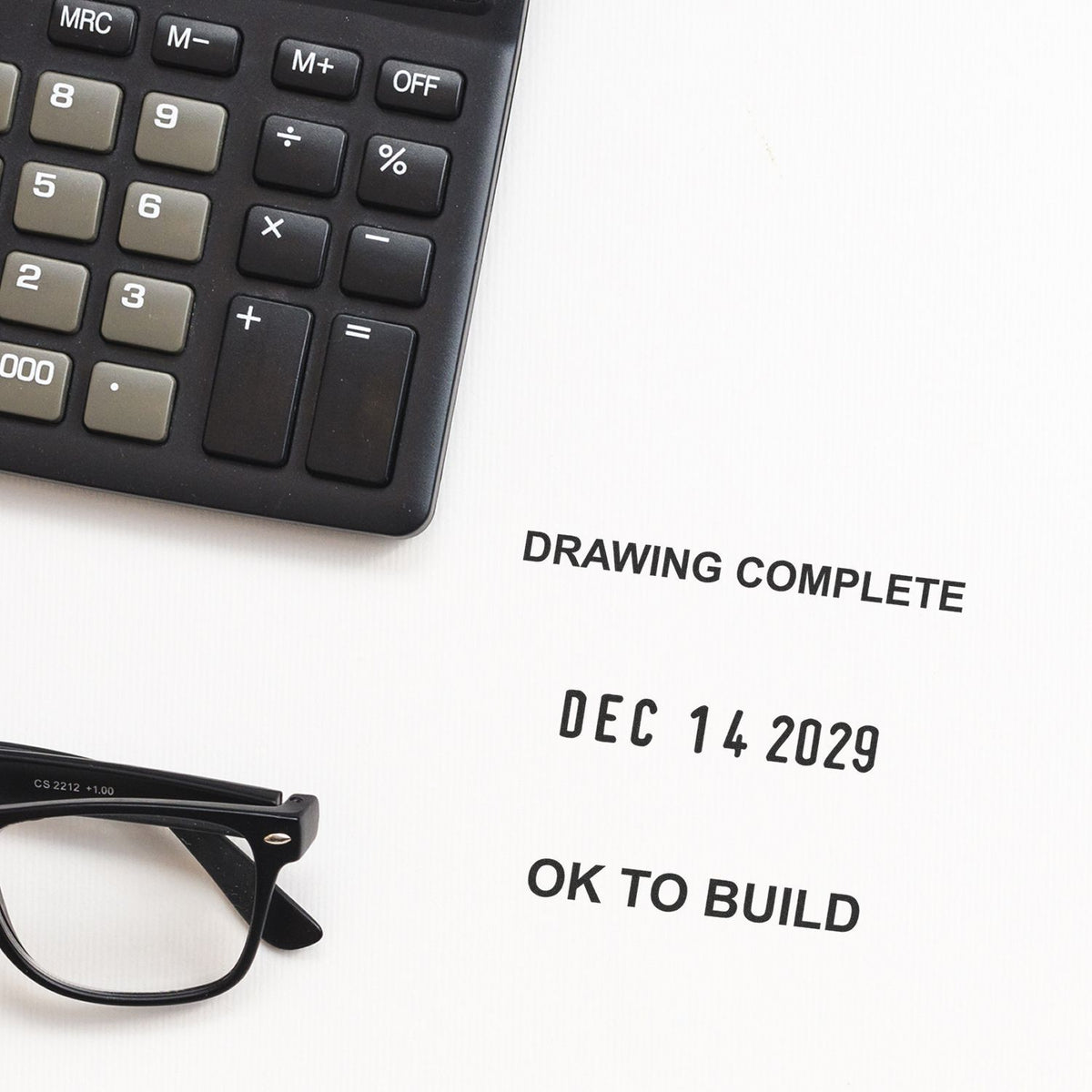 Calculator and eyeglasses on an engineering blueprint marked Drawing Complete and OK to Build with date Dec 14, 2029.