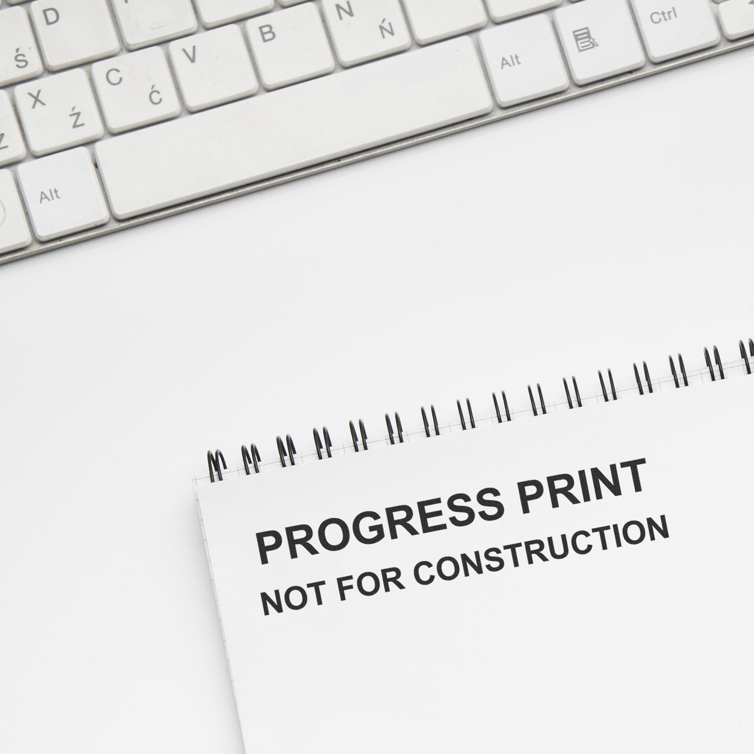 Keyboard beside progress print notebook labeled Not for Construction on a clean white desk.