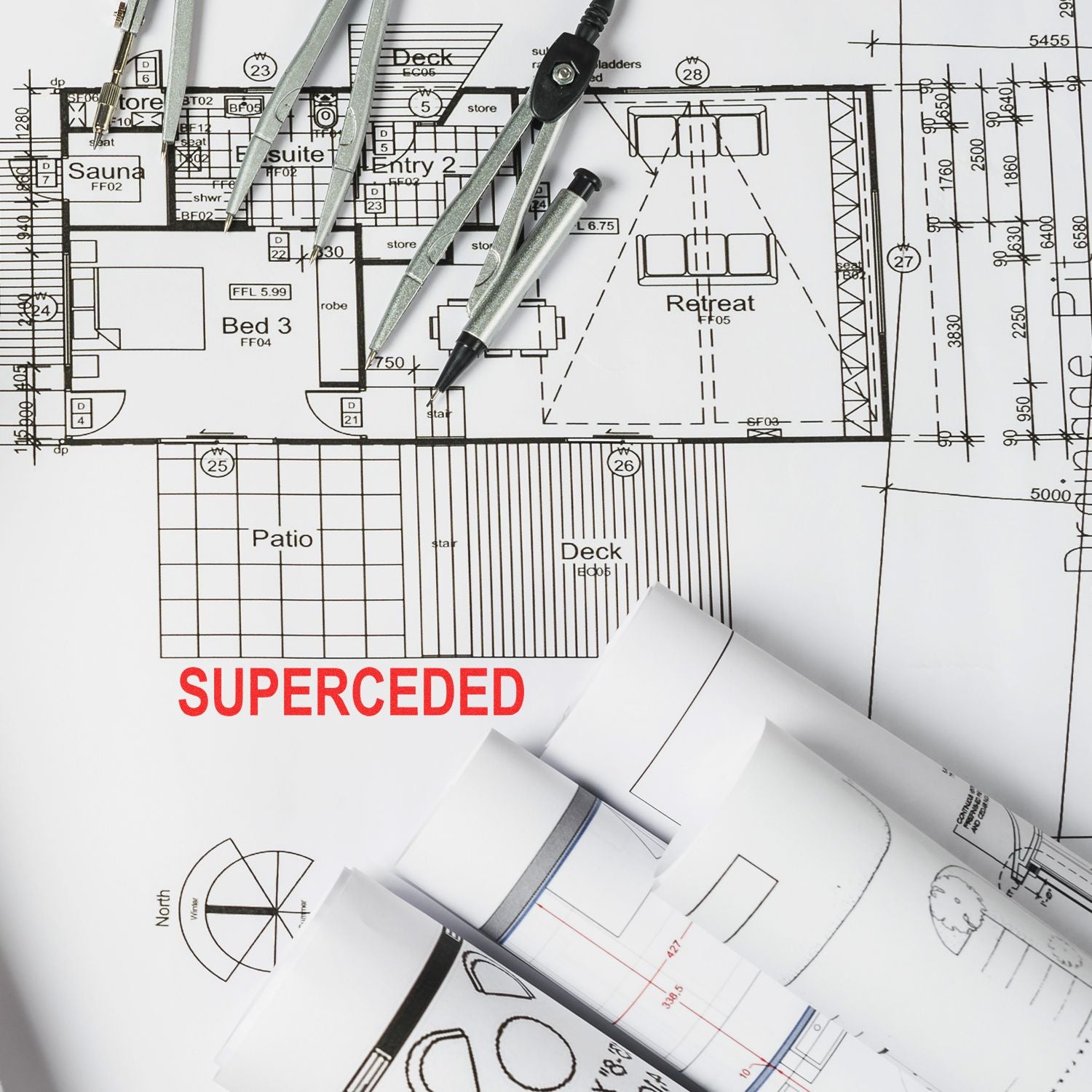 Architectural floor plans with drafting tools and rolled blueprints, marked SUPERCEDED on a house design drawing.