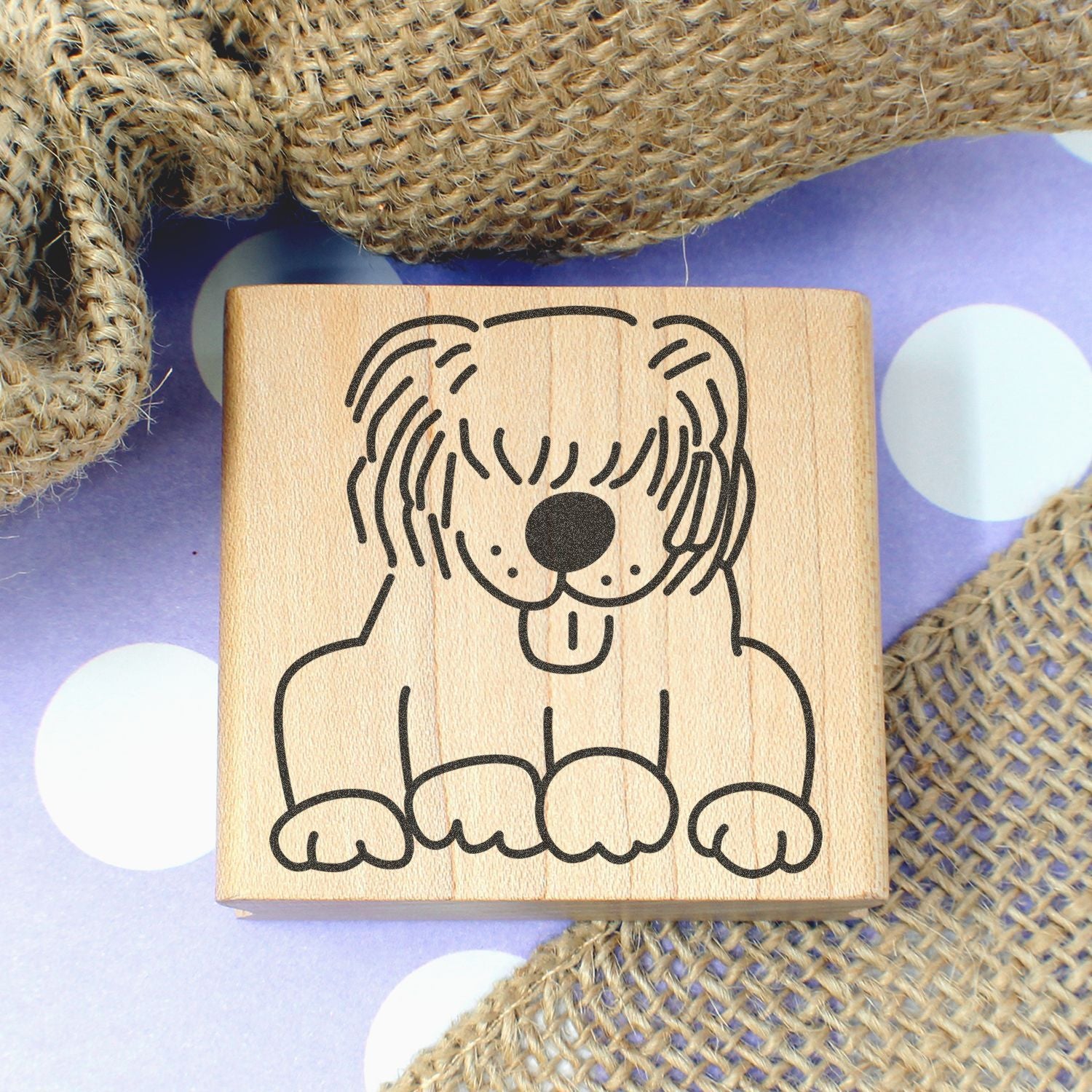 Cute dog stamp on wooden block with rustic burlap and purple polka dot background, handcrafted pet-themed design.