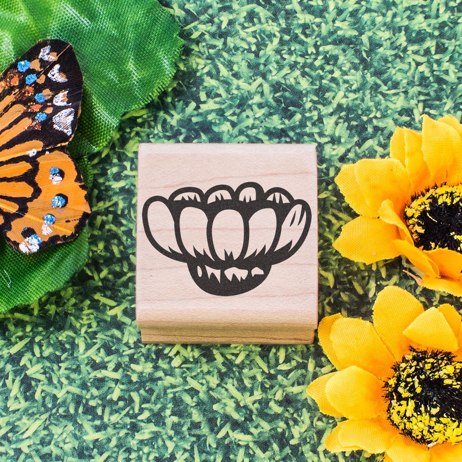 Wooden rubber stamp with flower design, butterfly wing, and bright yellow sunflower on green grass background