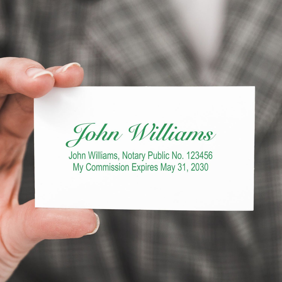 Hand holding John Williams notary public business card with green logo, license number 123456, and commission expiration date May 31, 2030.