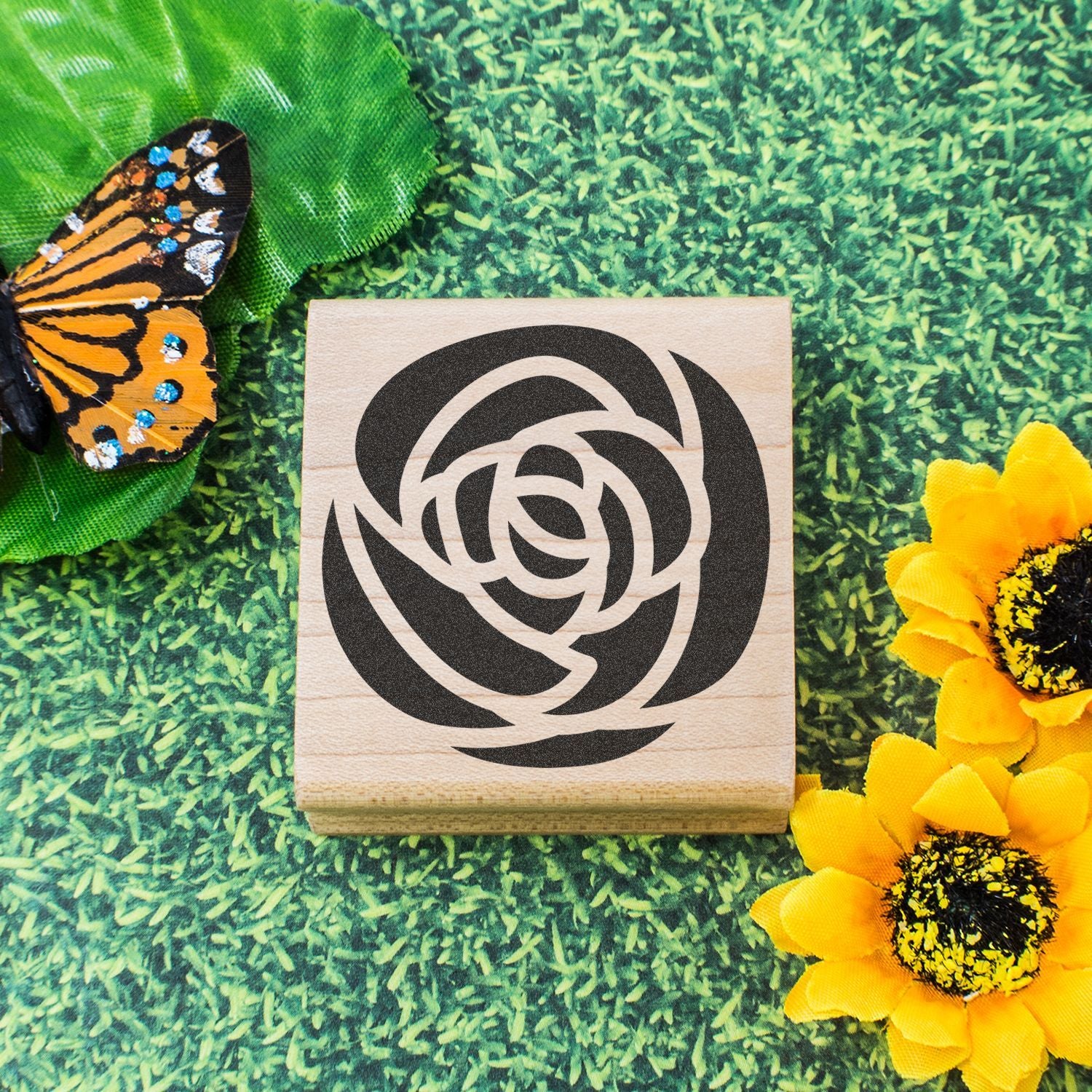 Wooden rose logo stamp on green grass background with butterfly and yellow sunflowers.