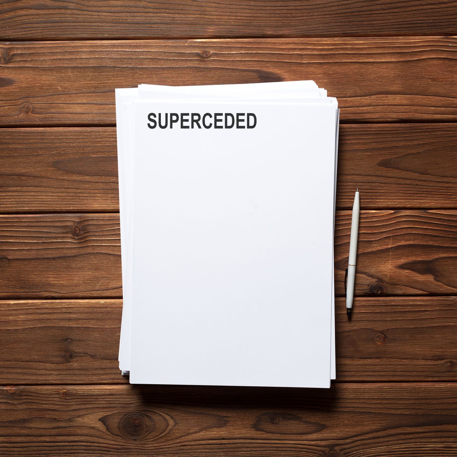 Stack of documents labeled SUPERCEDED on a wooden desk with a pen.