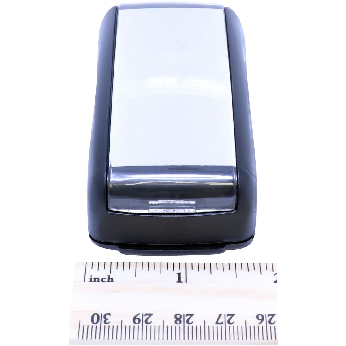 Close-up of compact black electronic device housing with chrome tip, shown next to inch ruler for size measurement.