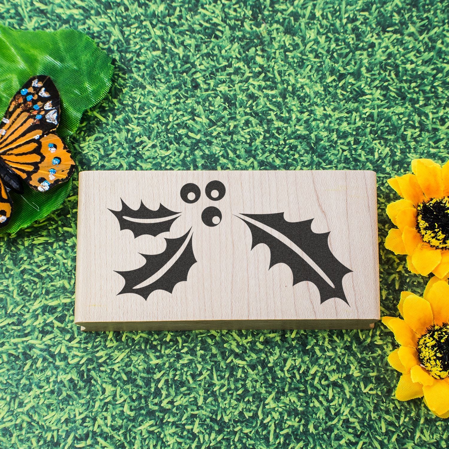 Decorative wooden sign with black bat silhouette on grass, surrounded by butterflies and sunflowers.