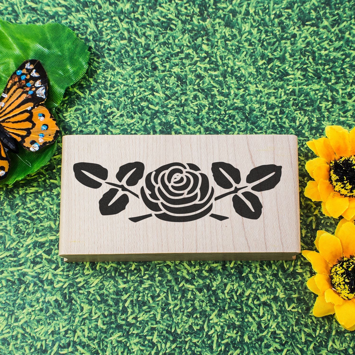 Wooden rose floral stencil sign on green grass with butterfly and sunflower decorations.