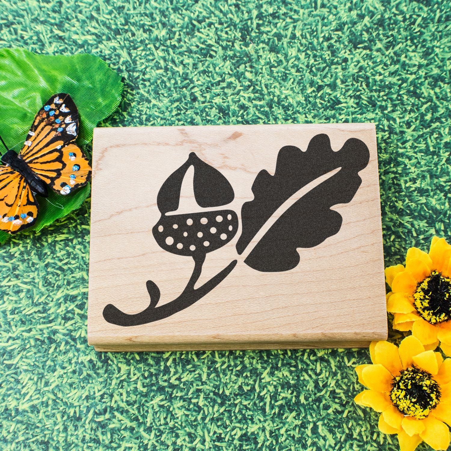 Decorative wooden acorn and oak leaf stamp on green grass with butterfly and sunflowers