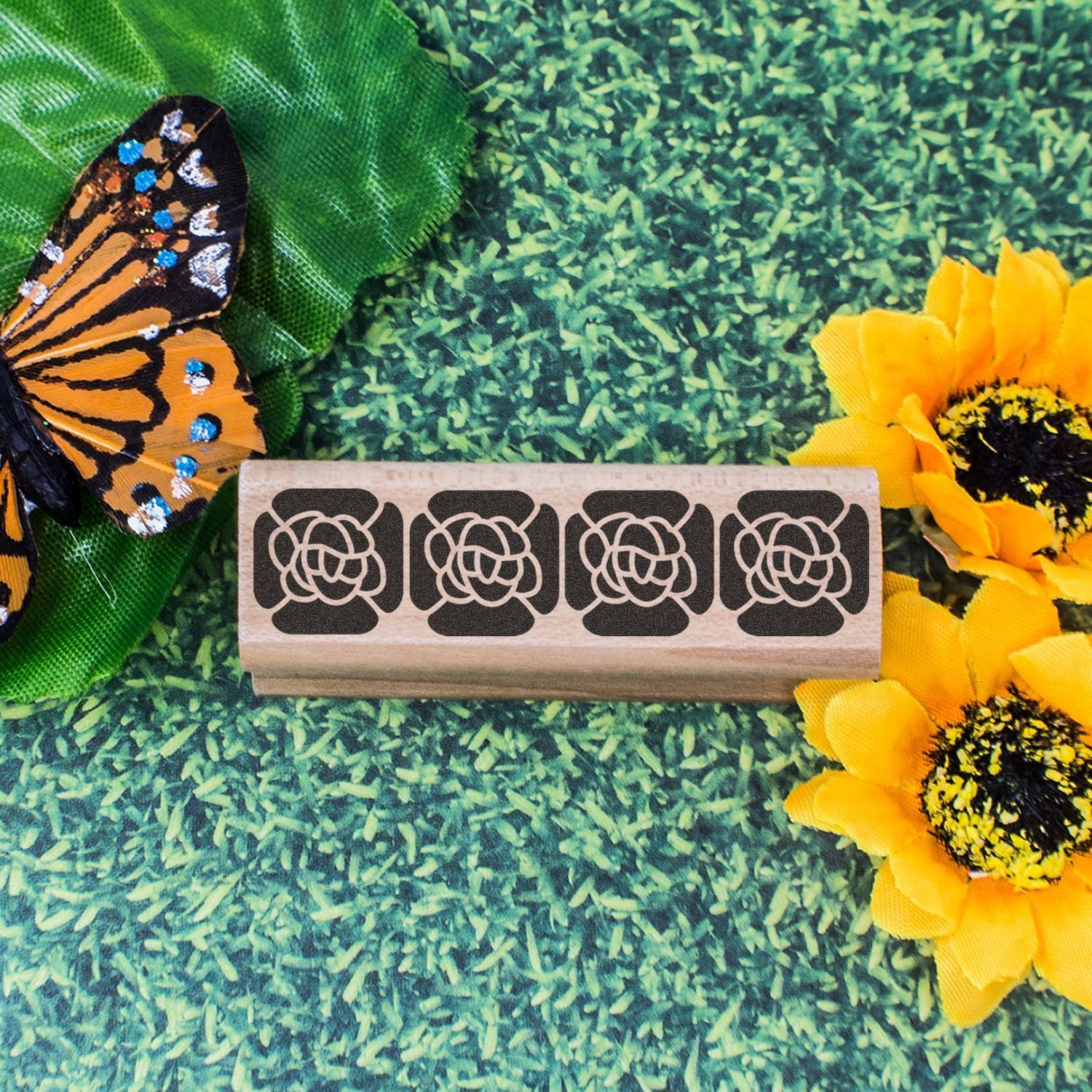 Decorative wooden floral stamp with butterfly wings and bright sunflowers on a green textured background.